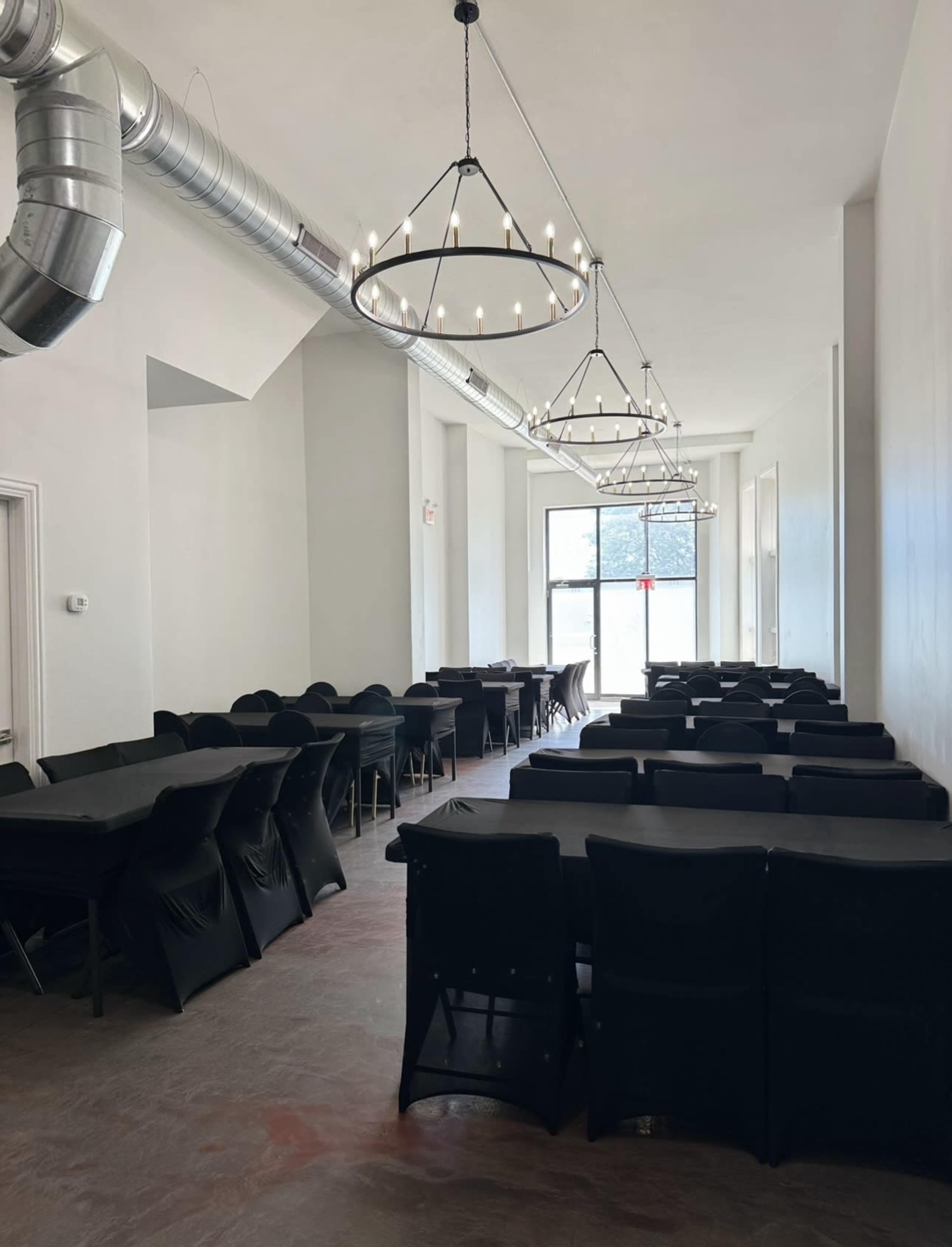 A spacious room with rows of black-covered tables and large light fixtures hanging from the ceiling.