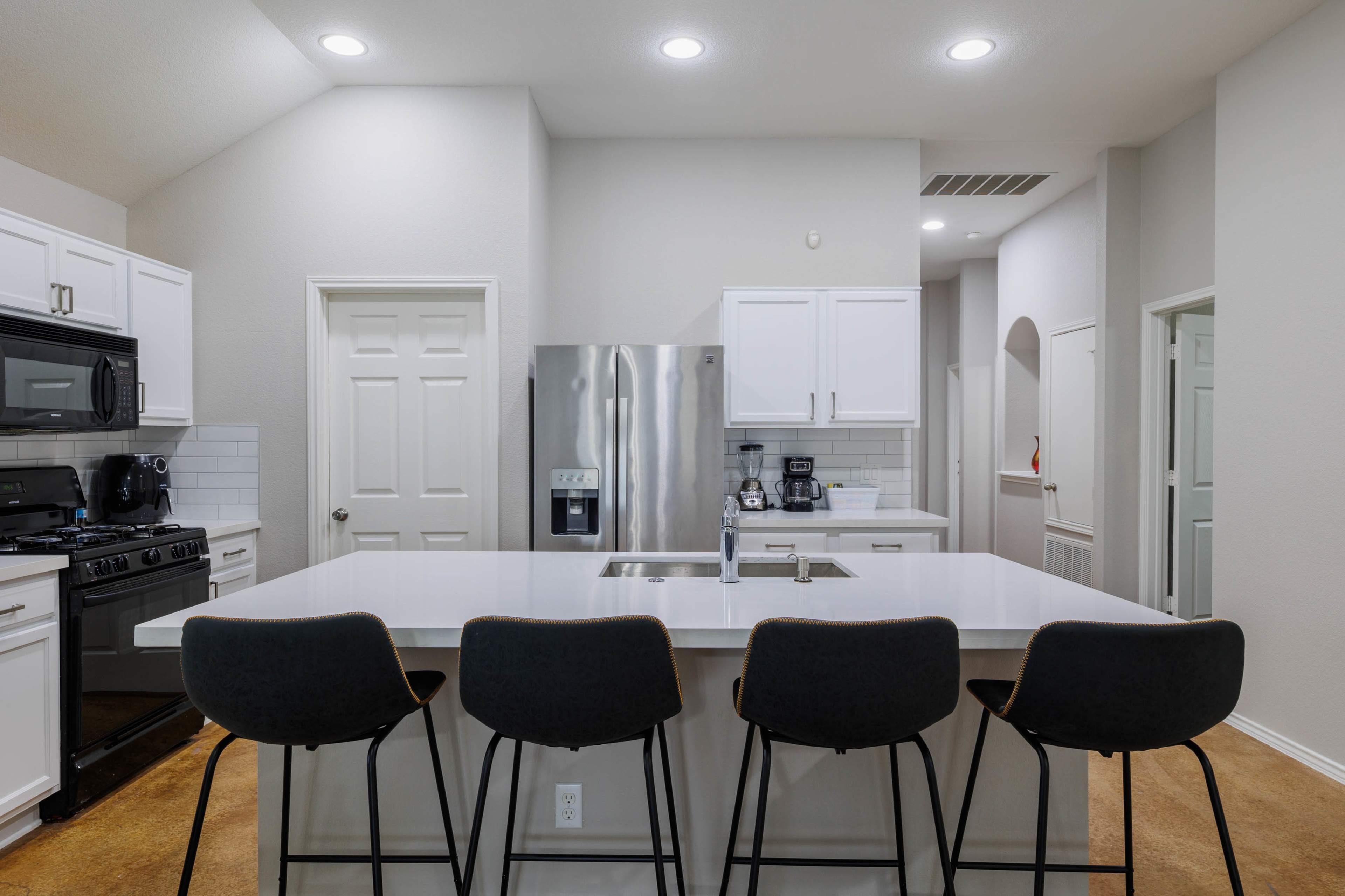 A modern kitchen features white cabinetry, stainless steel appliances, and a large island with four black bar stools.