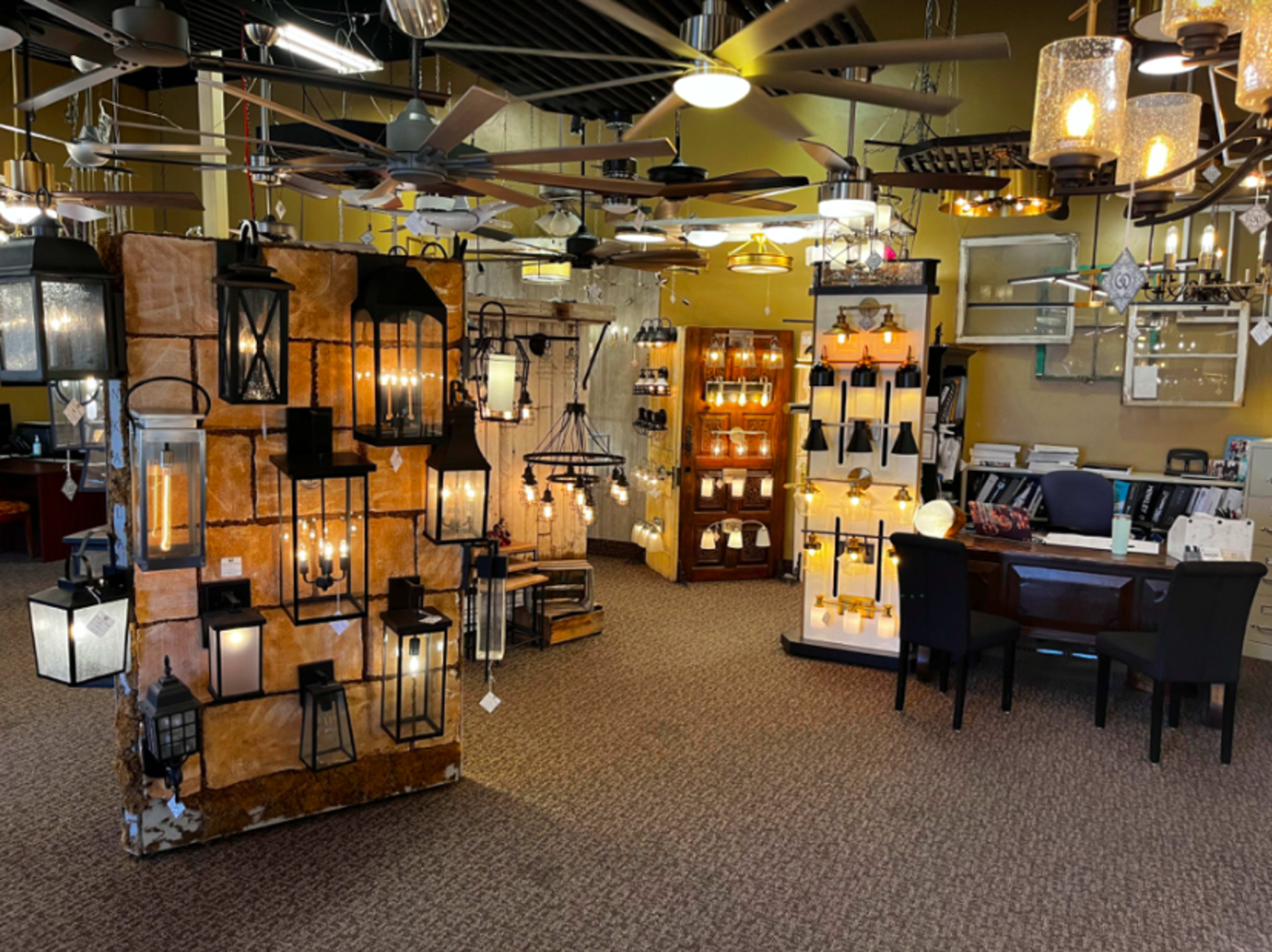 A lighting showroom featuring various hanging lamps and wall sconces displayed on structured panels, with a seating area and a desk visible in the background.