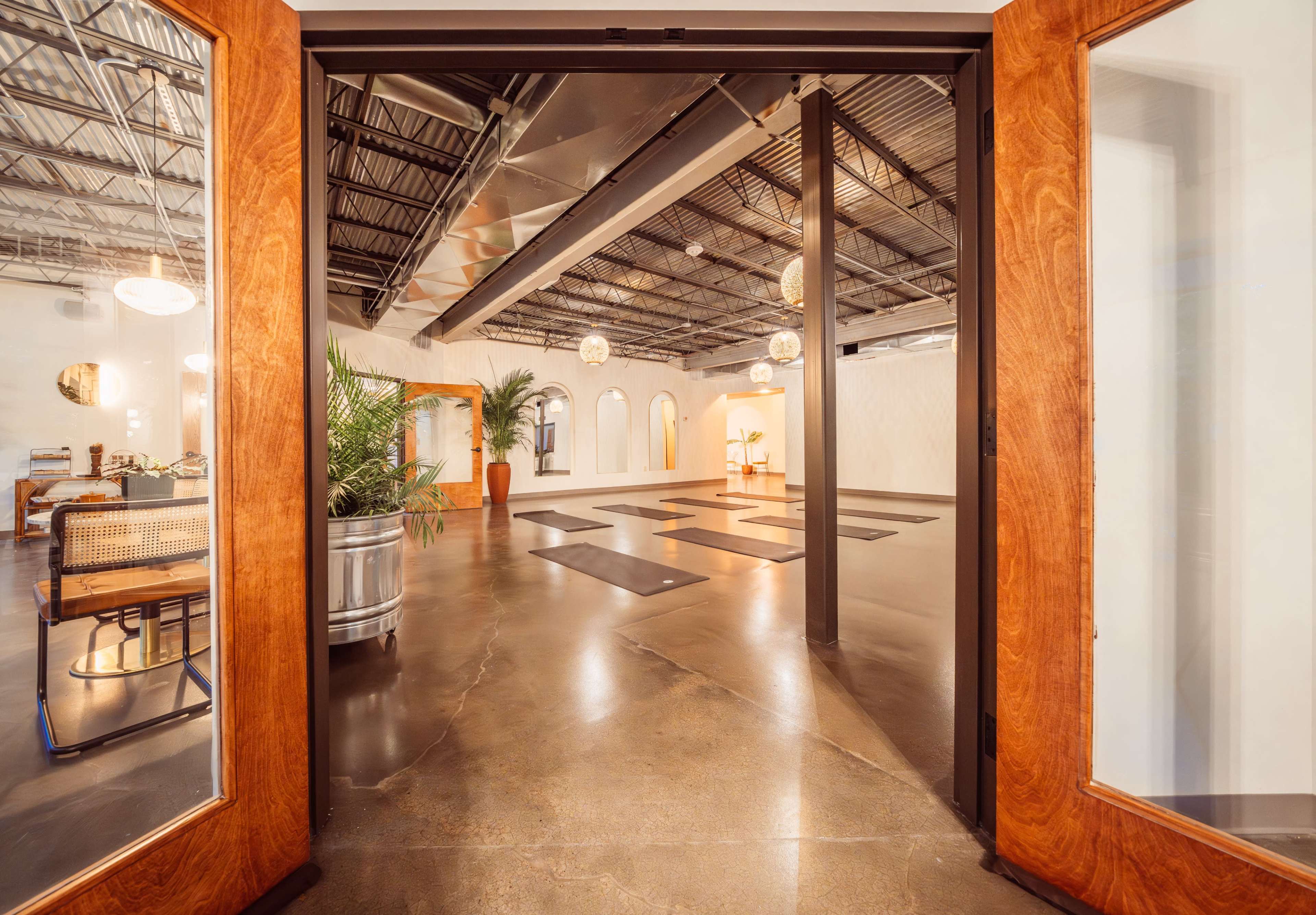 The image shows an open interior space with wooden double doors leading into a room featuring polished concrete floors, decorative lighting, and plants.