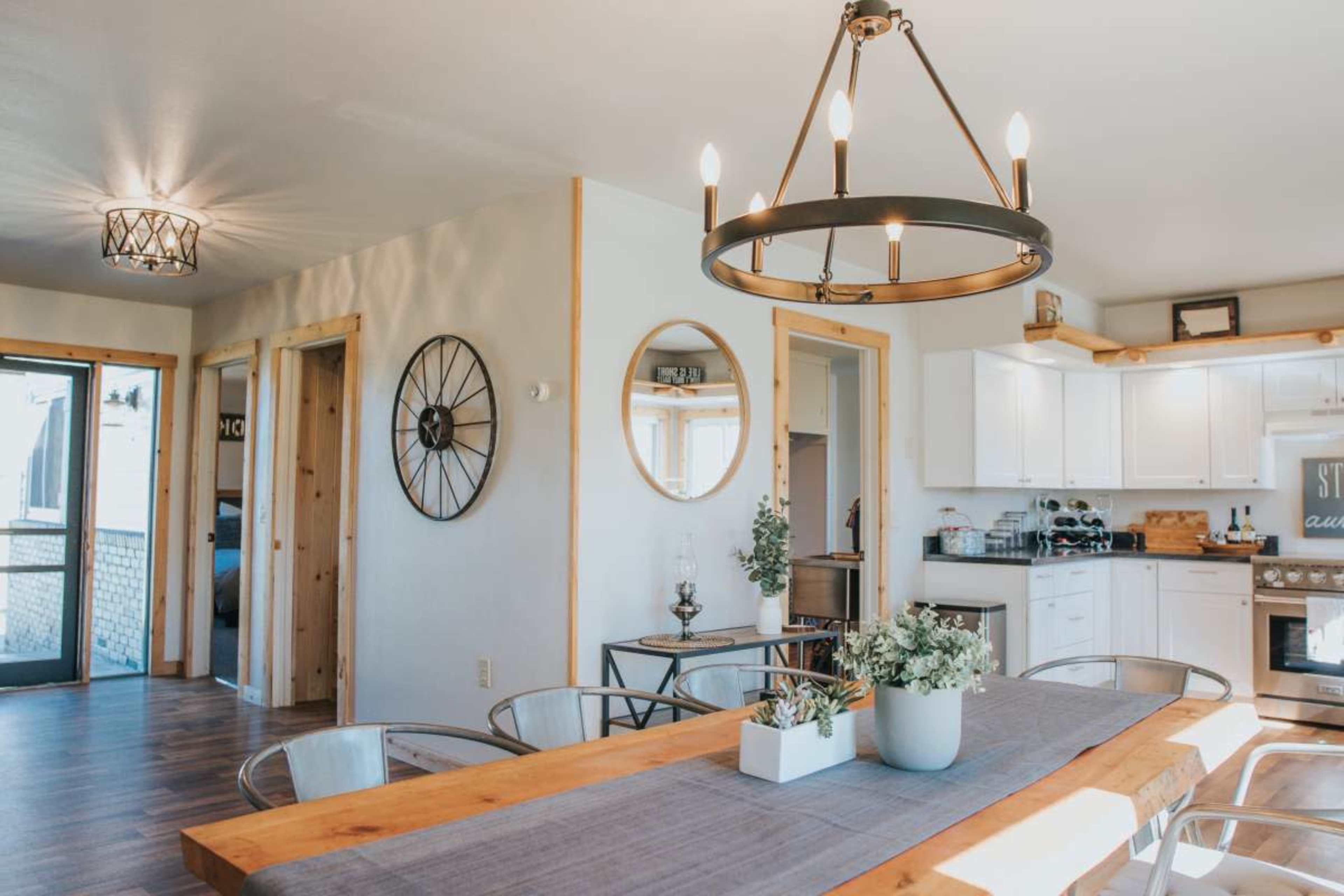The image features a modern kitchen and dining area with a large wooden table, circular lighting fixtures, and a mix of decorative elements.