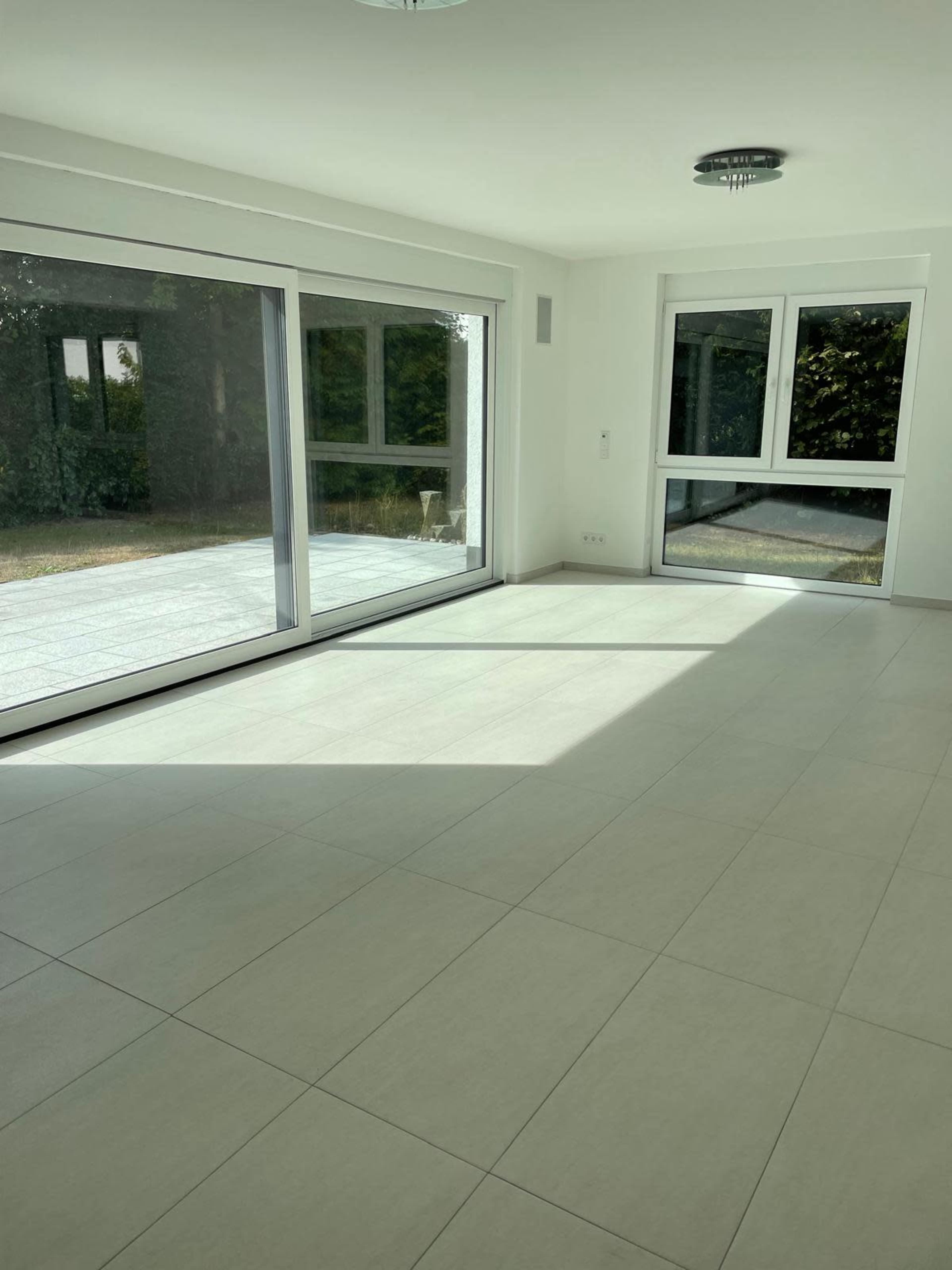 The image shows a bright, empty room with large windows that provide a view of the outdoors and flood the space with natural light.