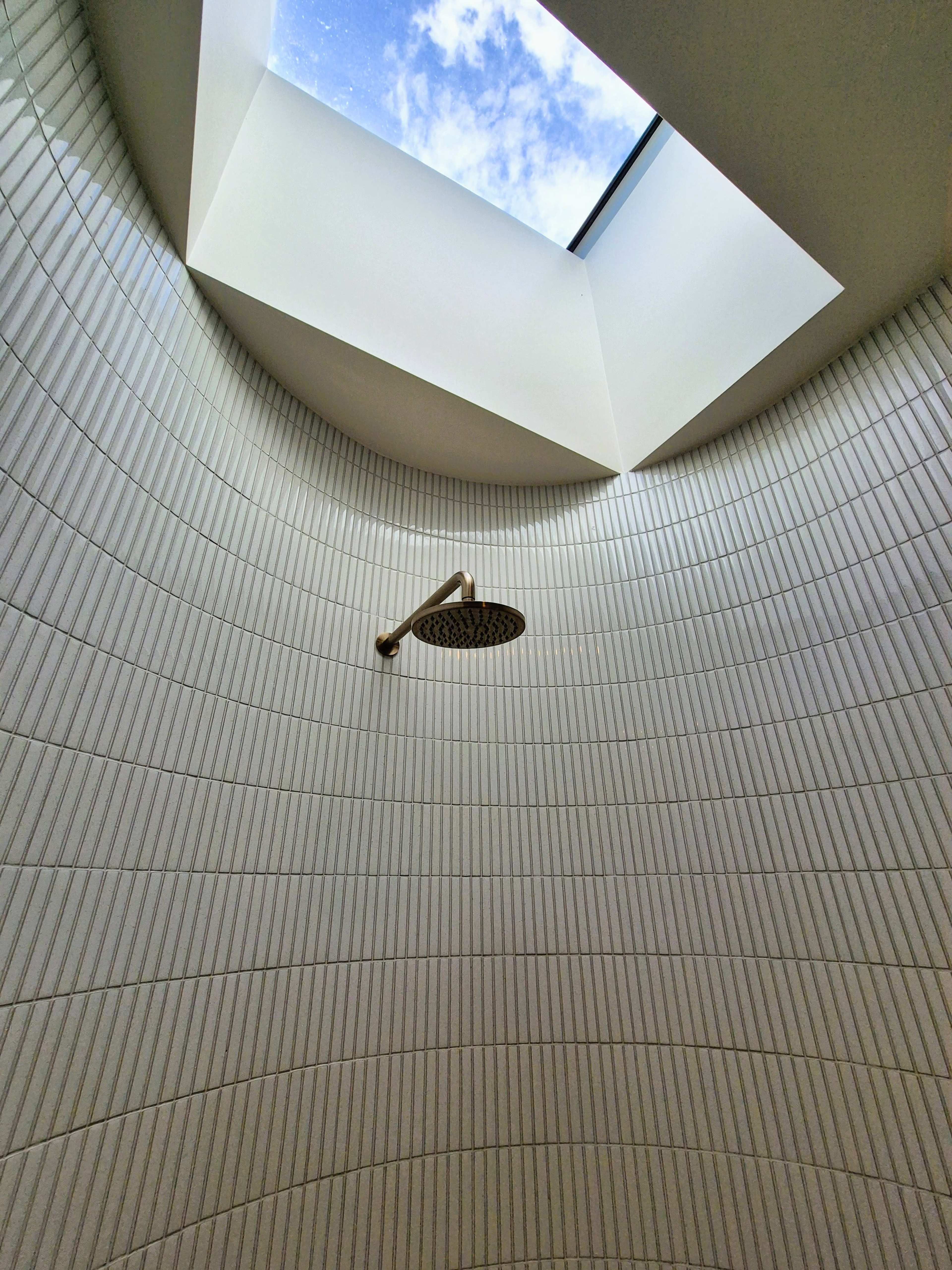 The image shows a modern shower area with a circular design and a skylight allowing natural light to enter.