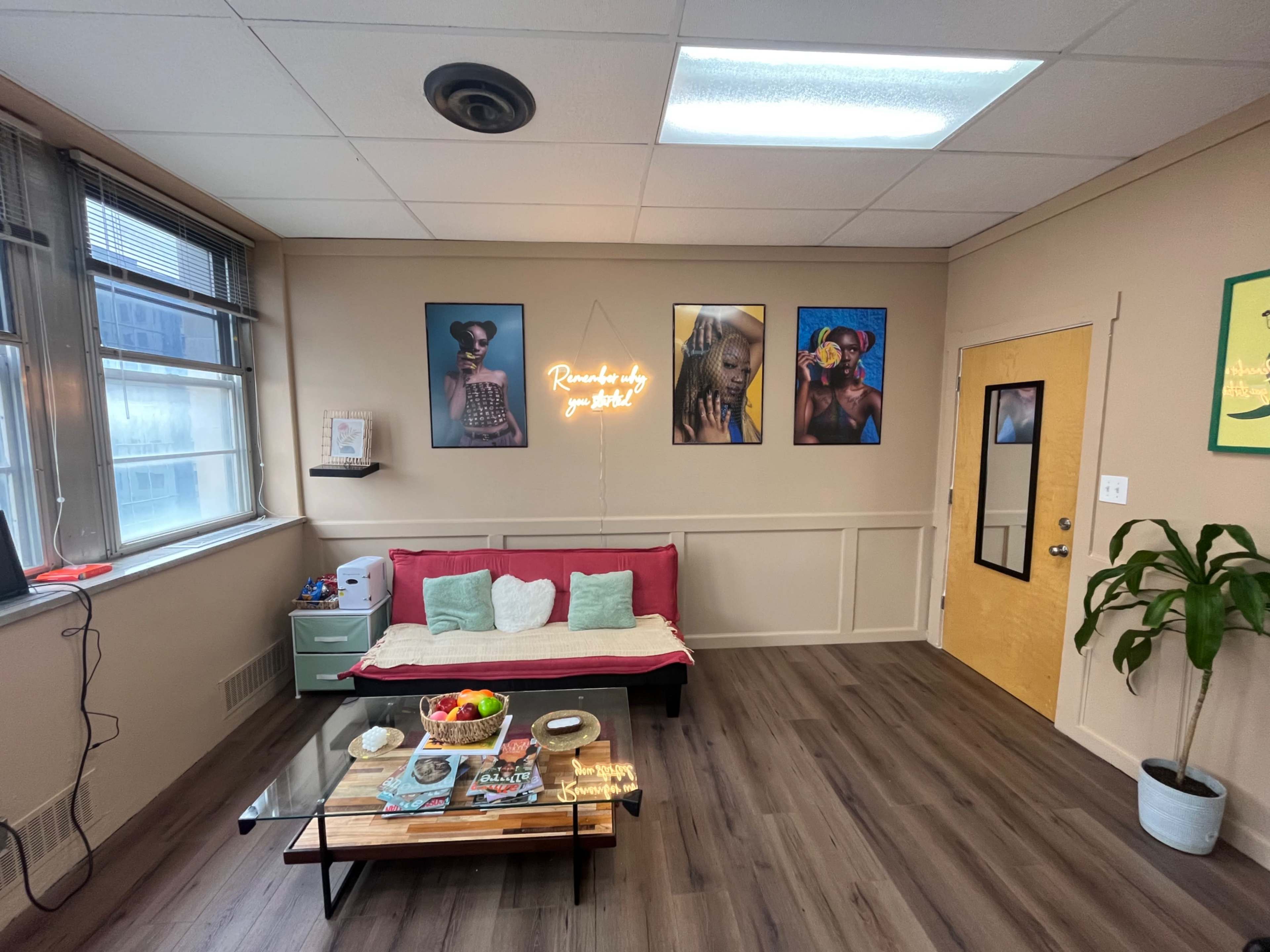 A cozy room featuring a red couch, a coffee table with snacks, and wall art, including vibrant posters, illuminated by a neon sign.