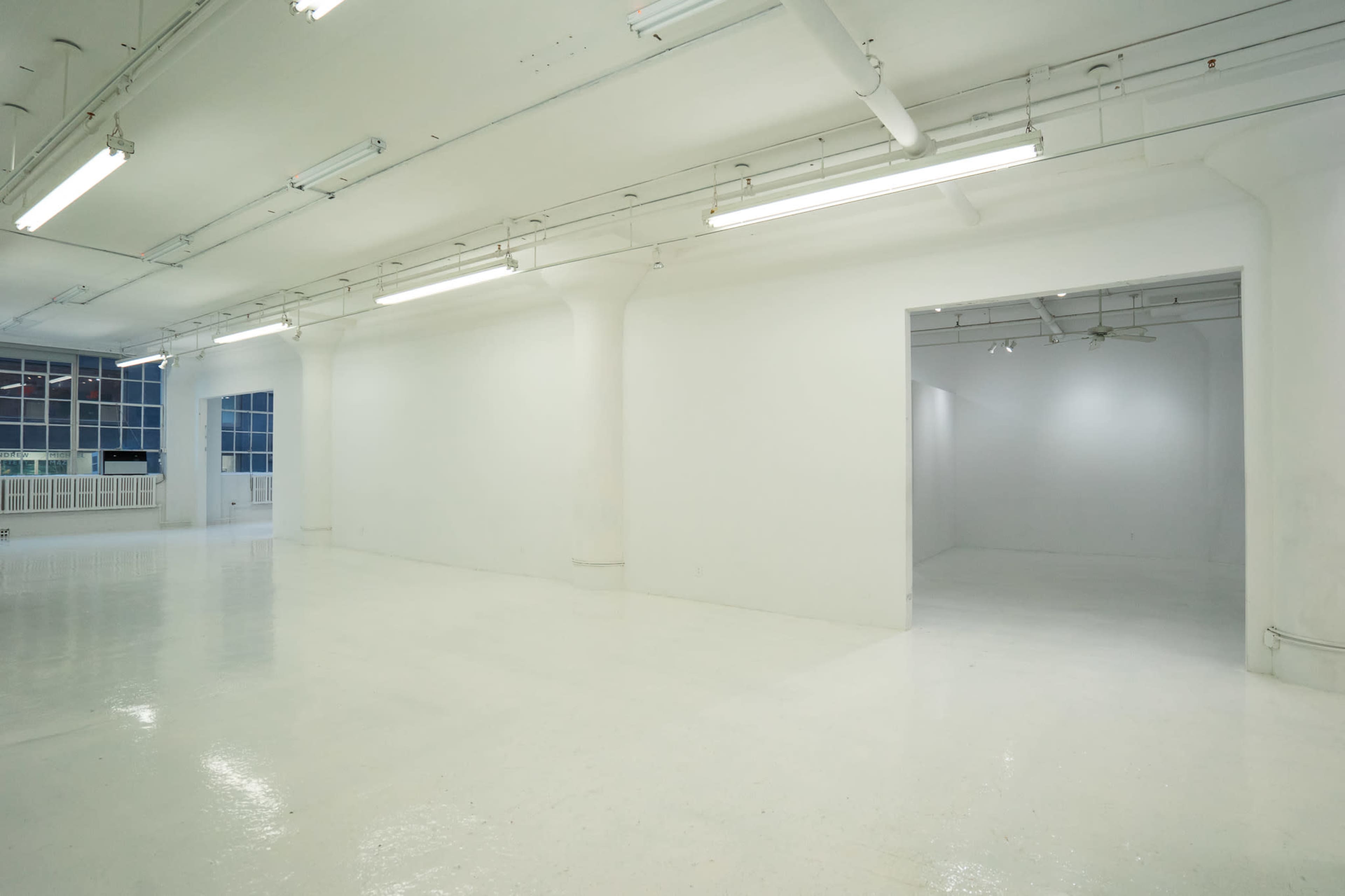 A vast, empty room with white walls and a glossy floor, illuminated by fluorescent lights.