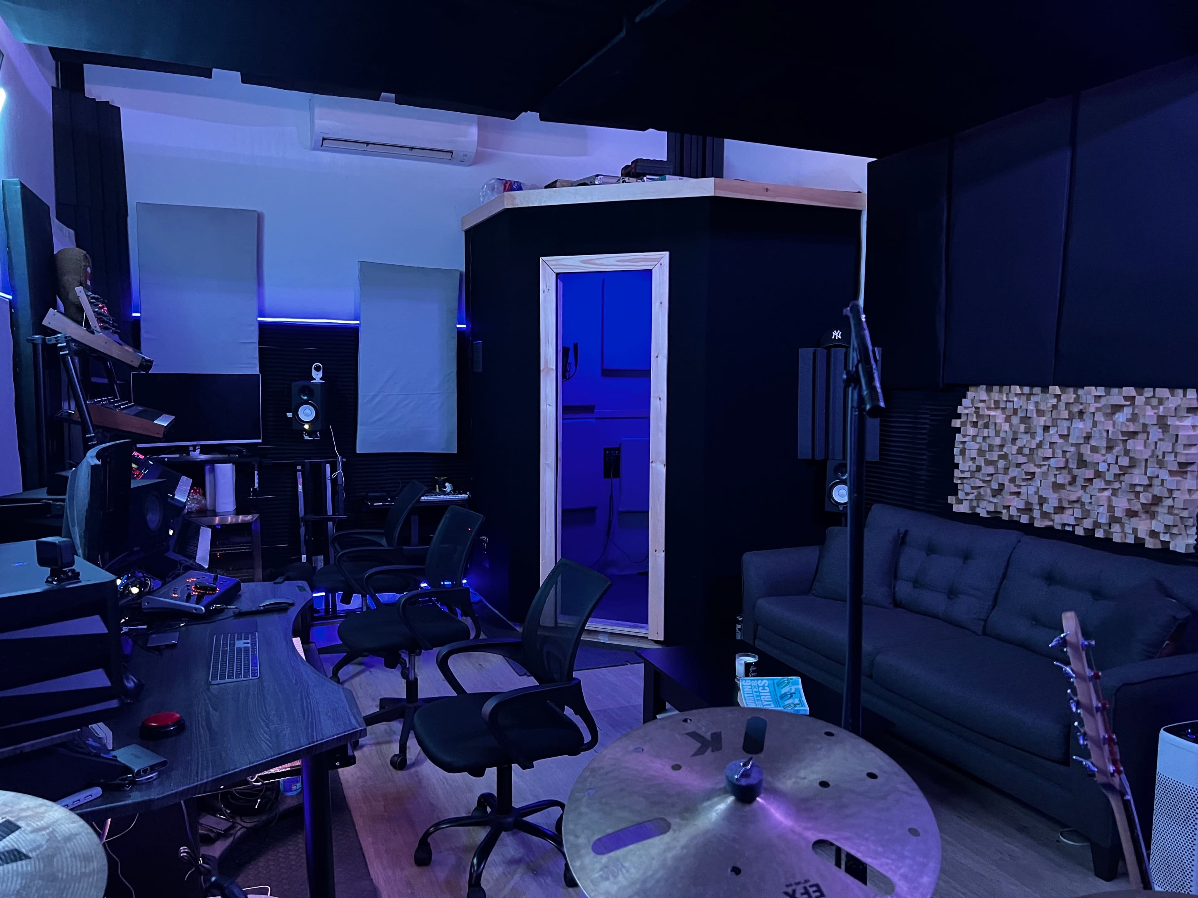 A music studio is equipped with various instruments, recording equipment, and soundproofing materials, featuring a separate vocal booth.