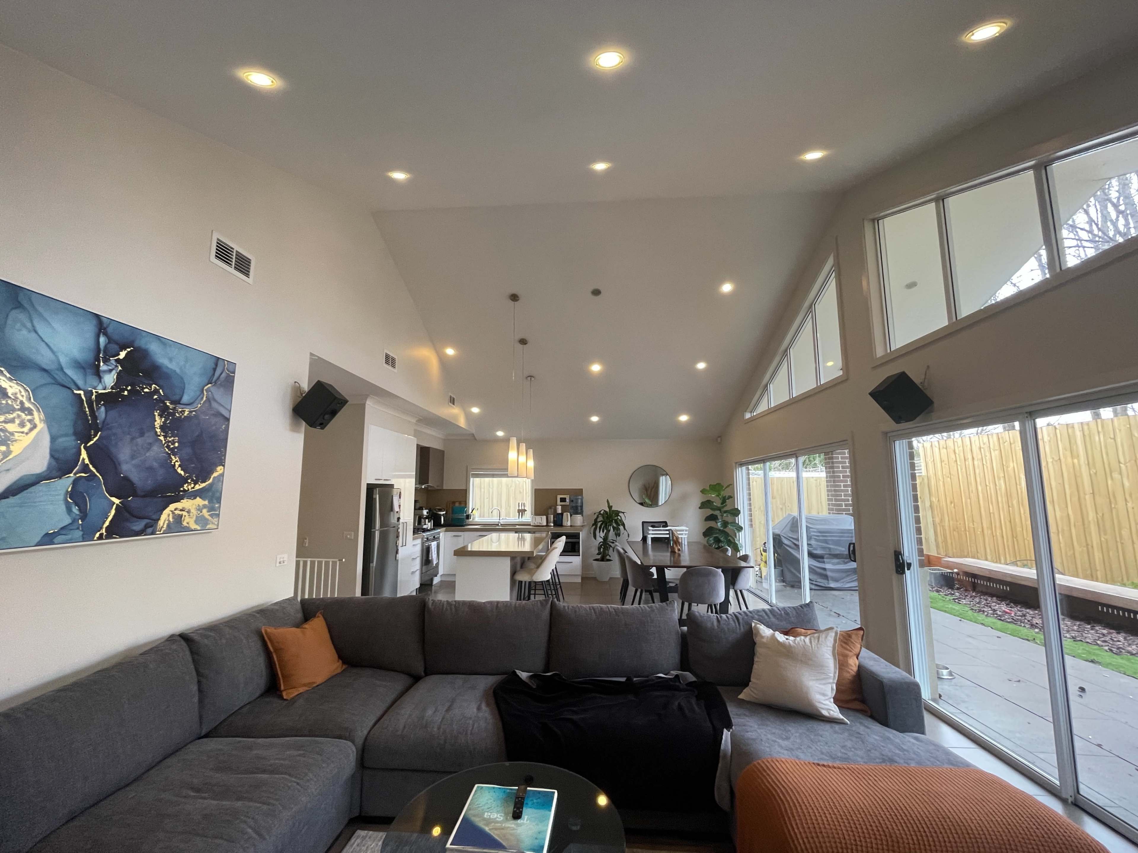 A modern living room with a large sectional sofa, a coffee table, and a view of an open kitchen and dining area, featuring large windows that let in natural light.