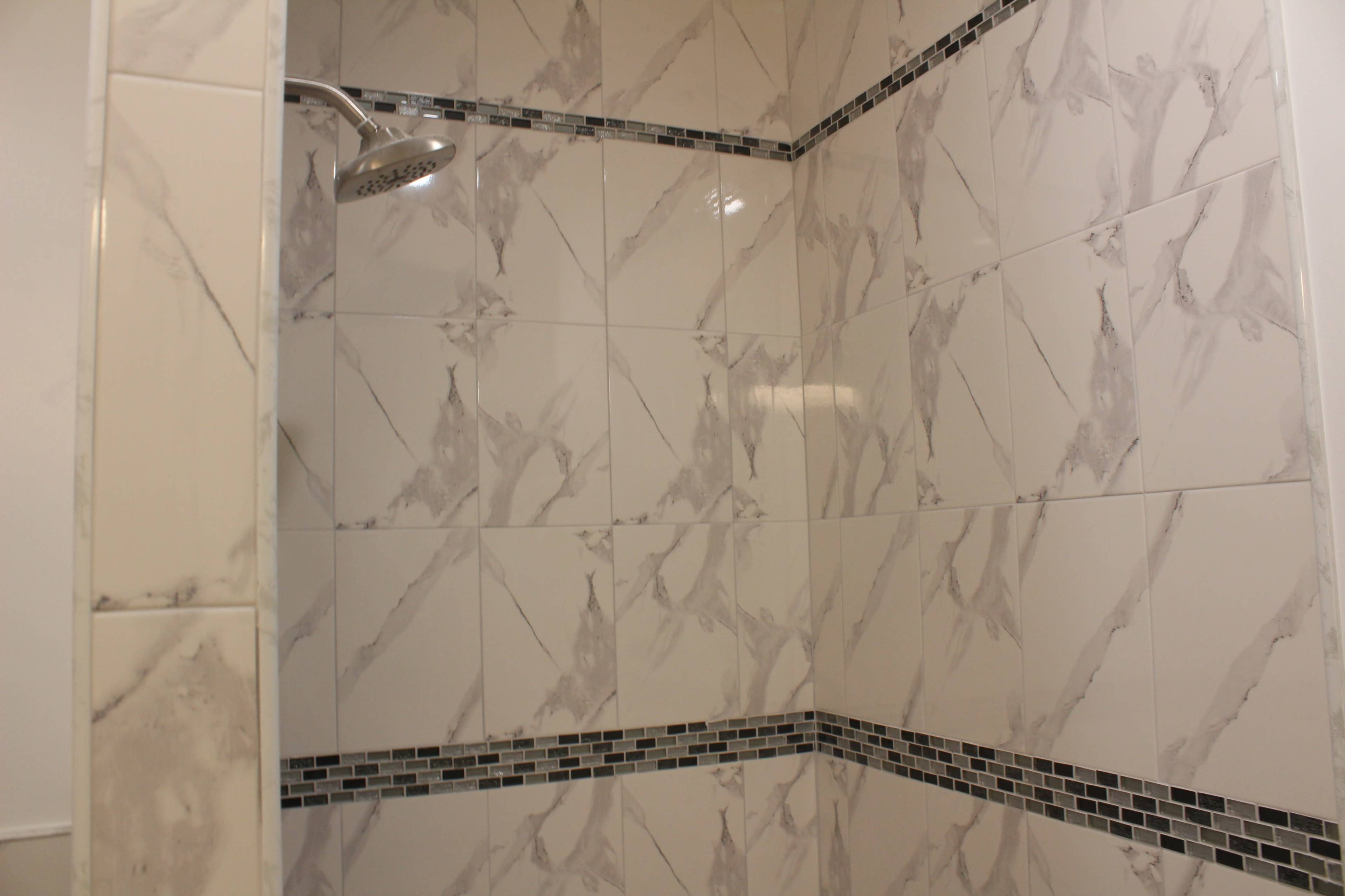 The image shows a modern tiled shower with gray and white marbled tiles and a mosaic border.