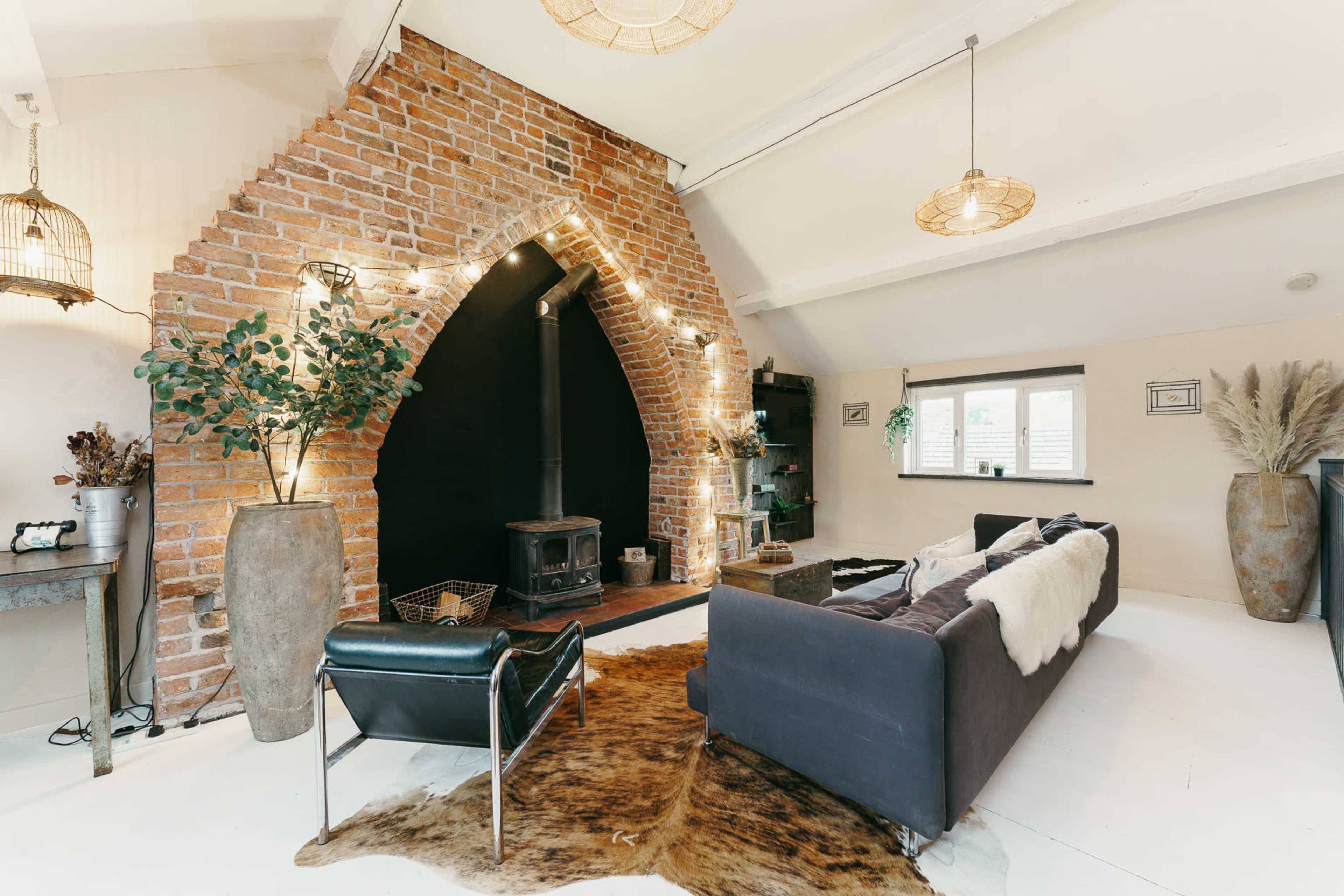 The image features a living space with a large brick archway, a black wood stove, and a sofa arranged near a decorative cowhide rug.