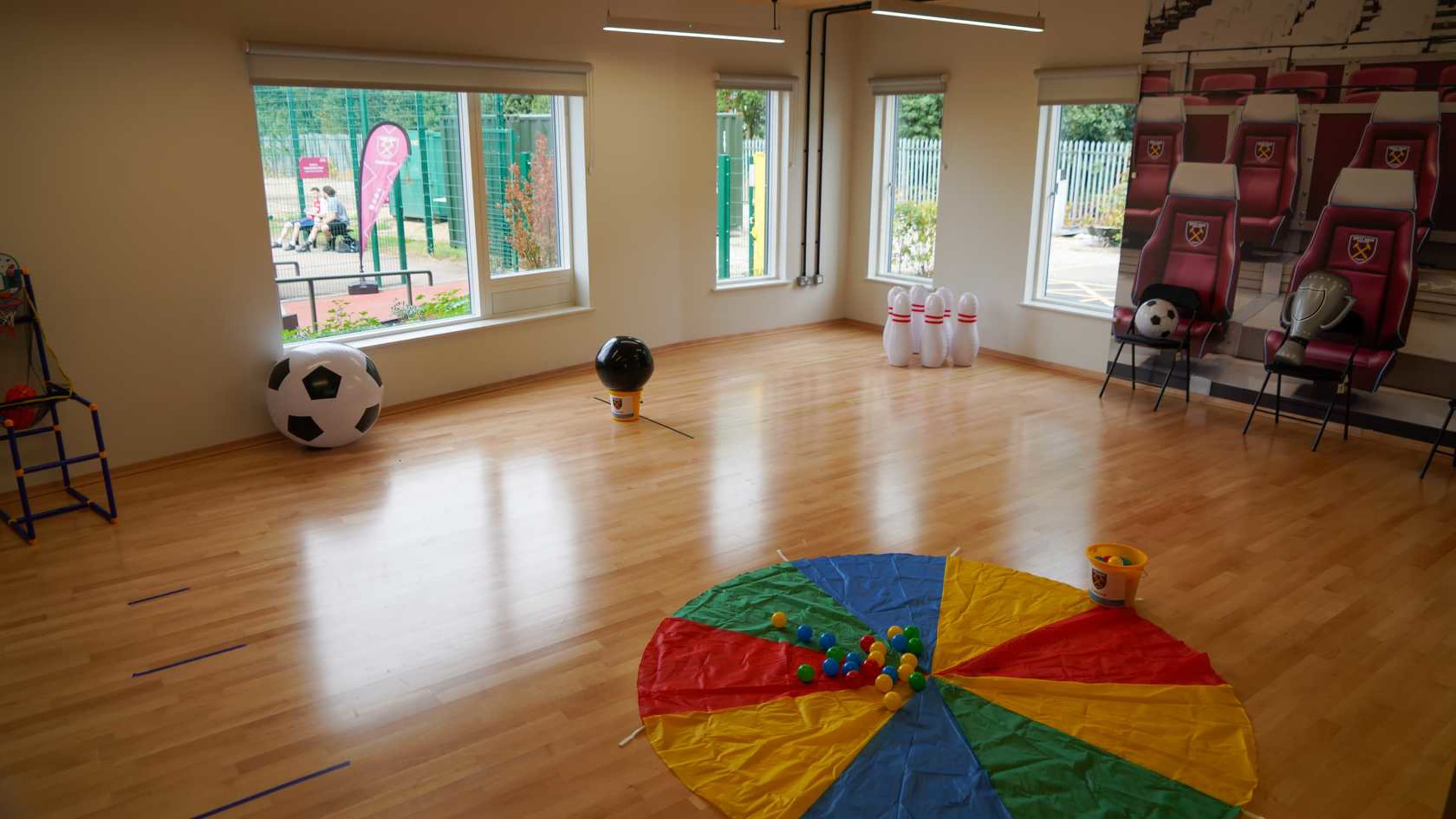 The room has wooden flooring and is furnished with various sports-themed items, including a large soccer ball, bowling pins, and a colorful parachute with balls in the center.