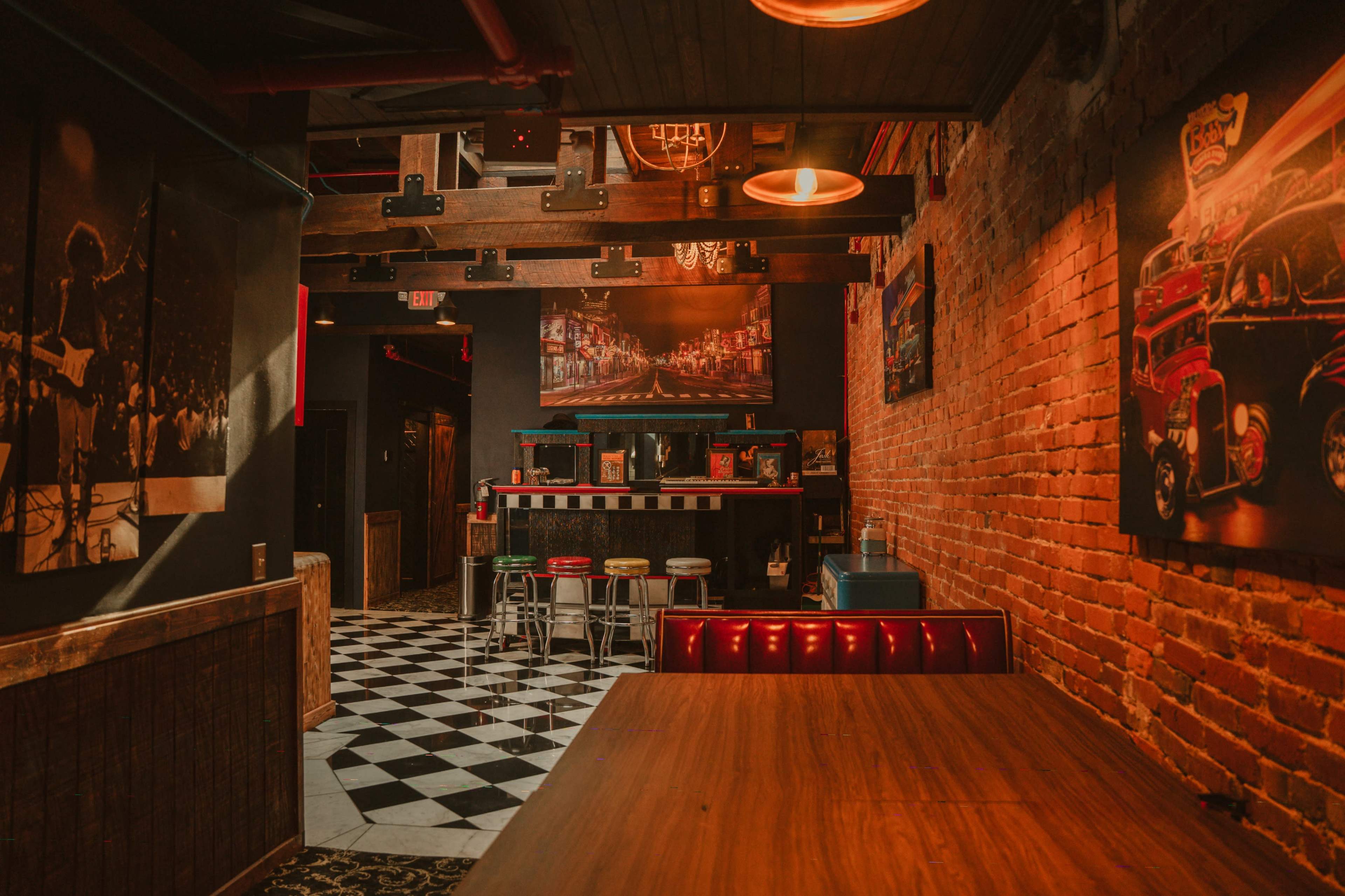 The image shows a dimly lit bar area with a checkered floor, exposed brick walls, and various artworks on display.