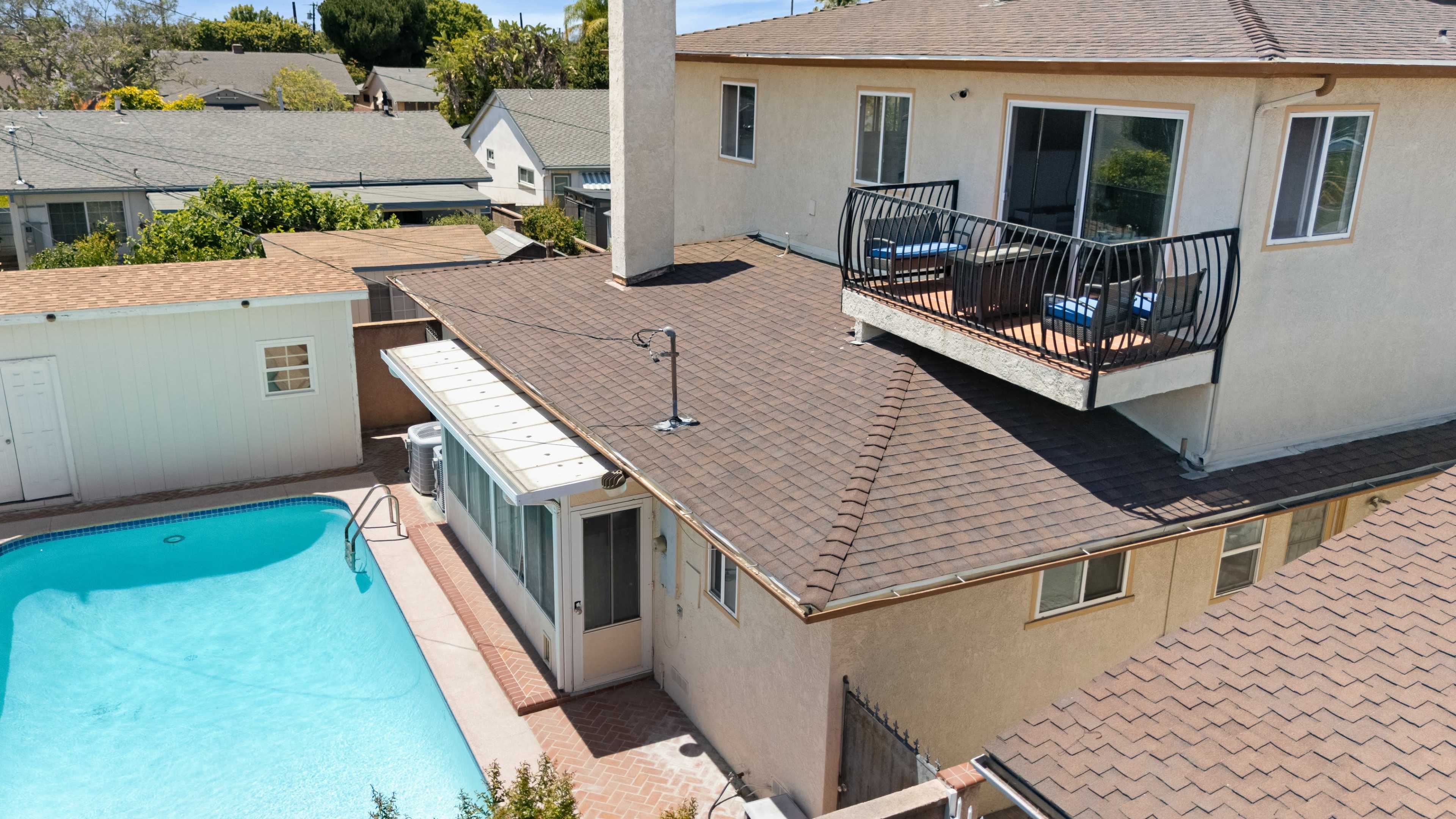 The image shows a house with a swimming pool in the backyard, featuring a shaded patio area and a balcony on the upper level.