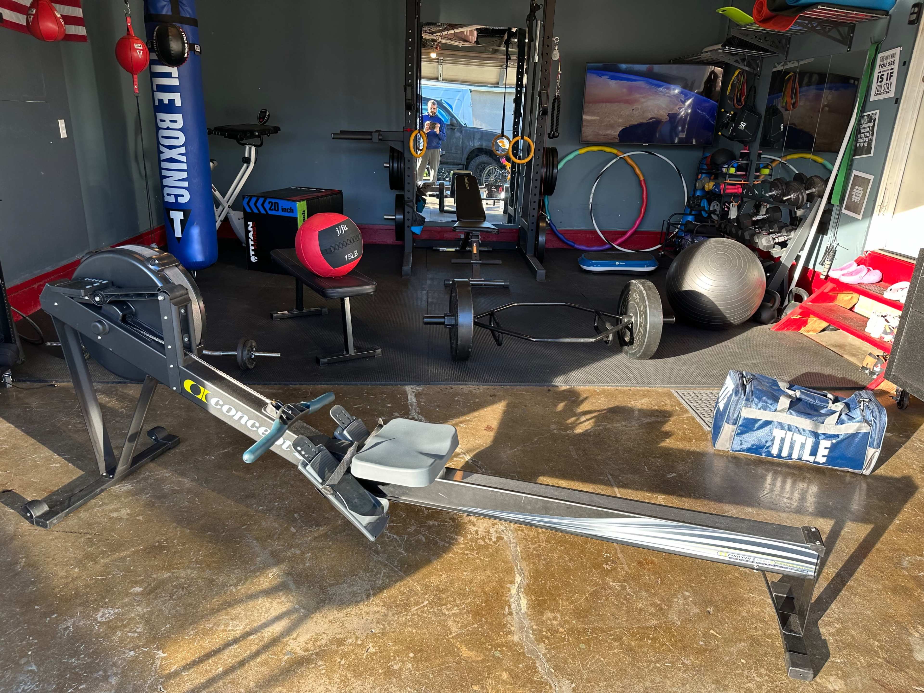 A gym with various fitness equipment including a rowing machine, weights, yoga balls, and boxing gear.