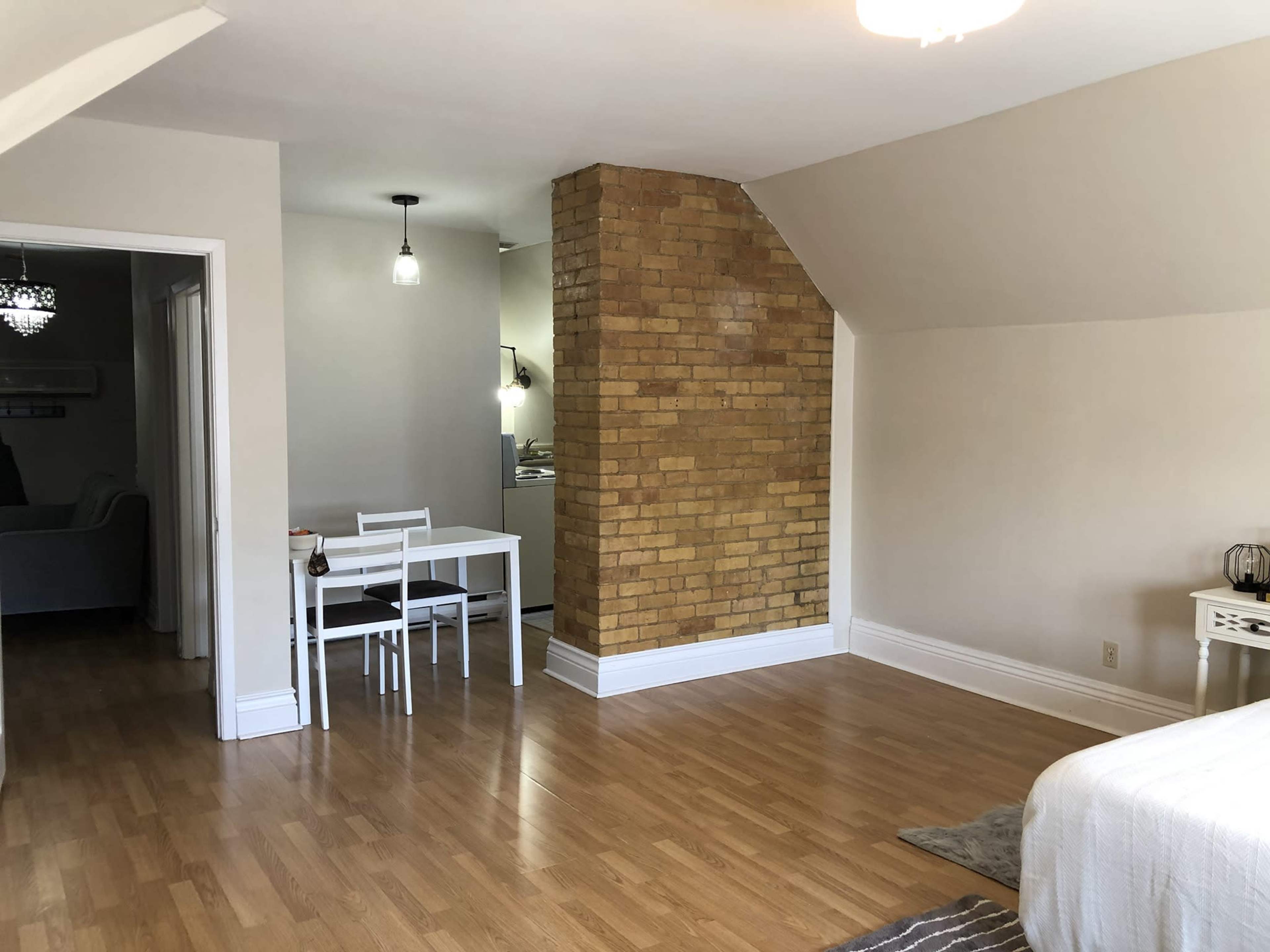 A spacious room featuring a wooden floor, a textured brick wall, and a dining area with a table and chairs in the background.