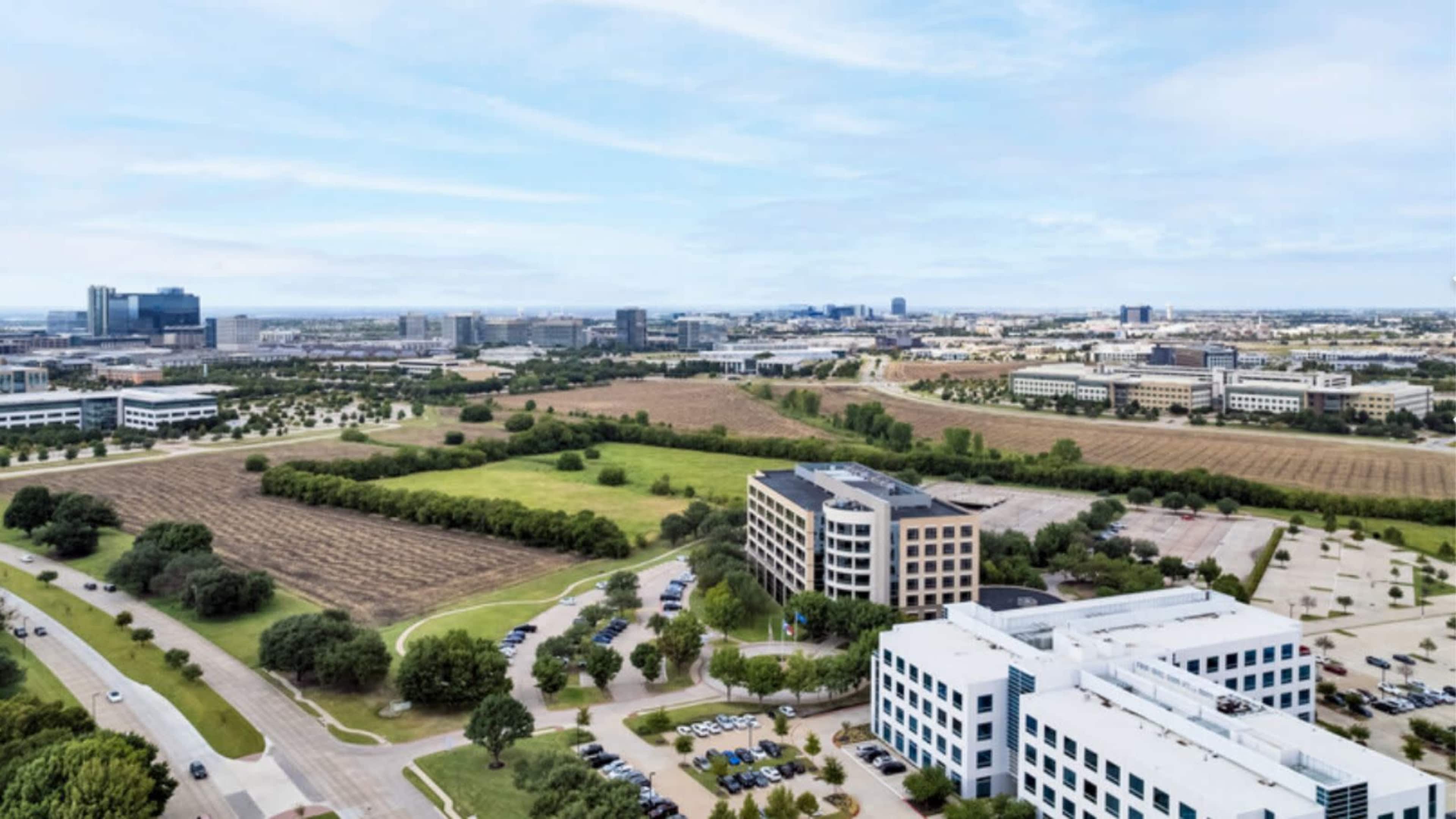 The image shows a panoramic view of a suburban business district with multiple office buildings and green fields.