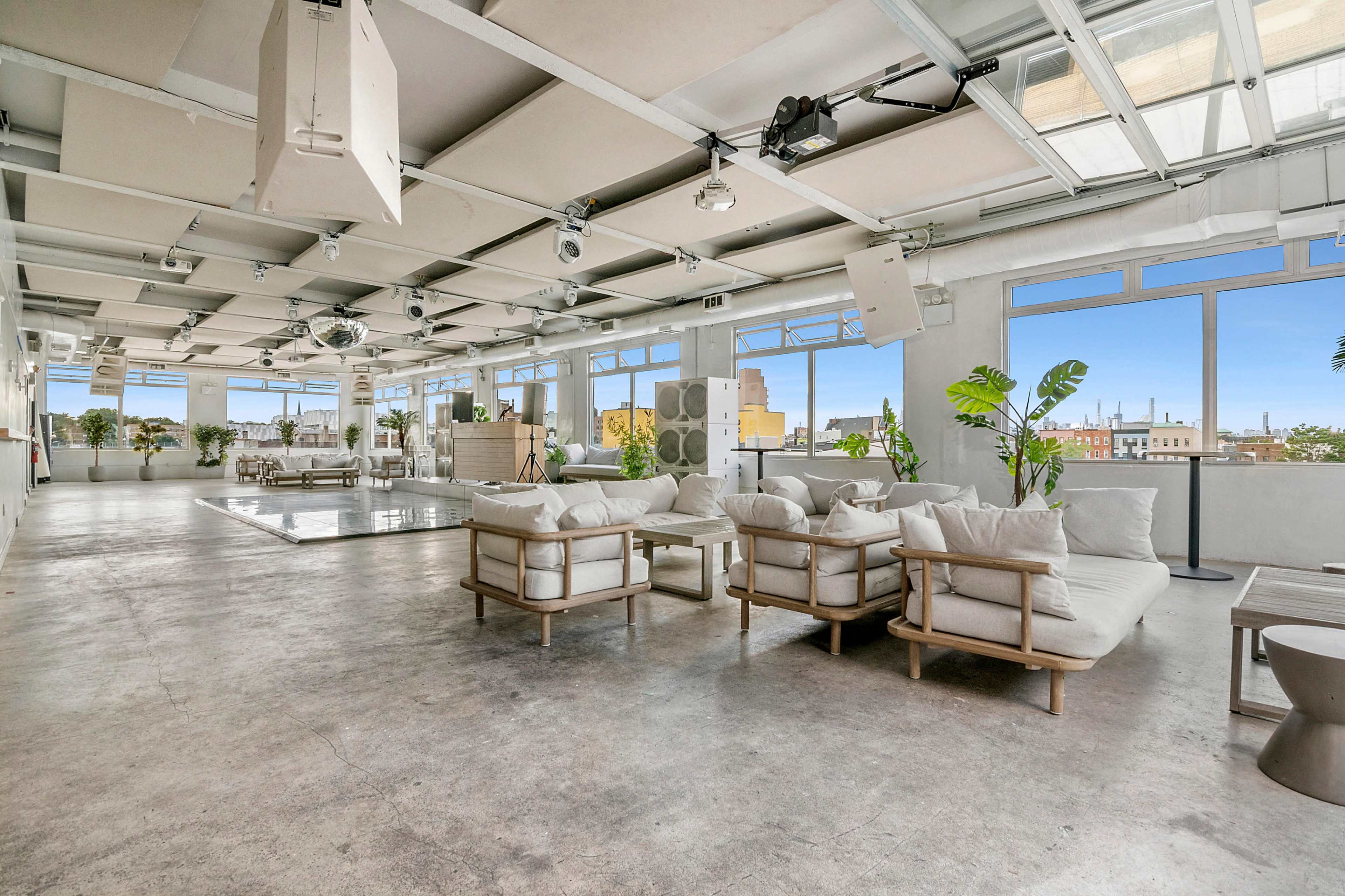 The image shows a spacious, modern interior with light-colored furniture, large windows, and a minimalist design.