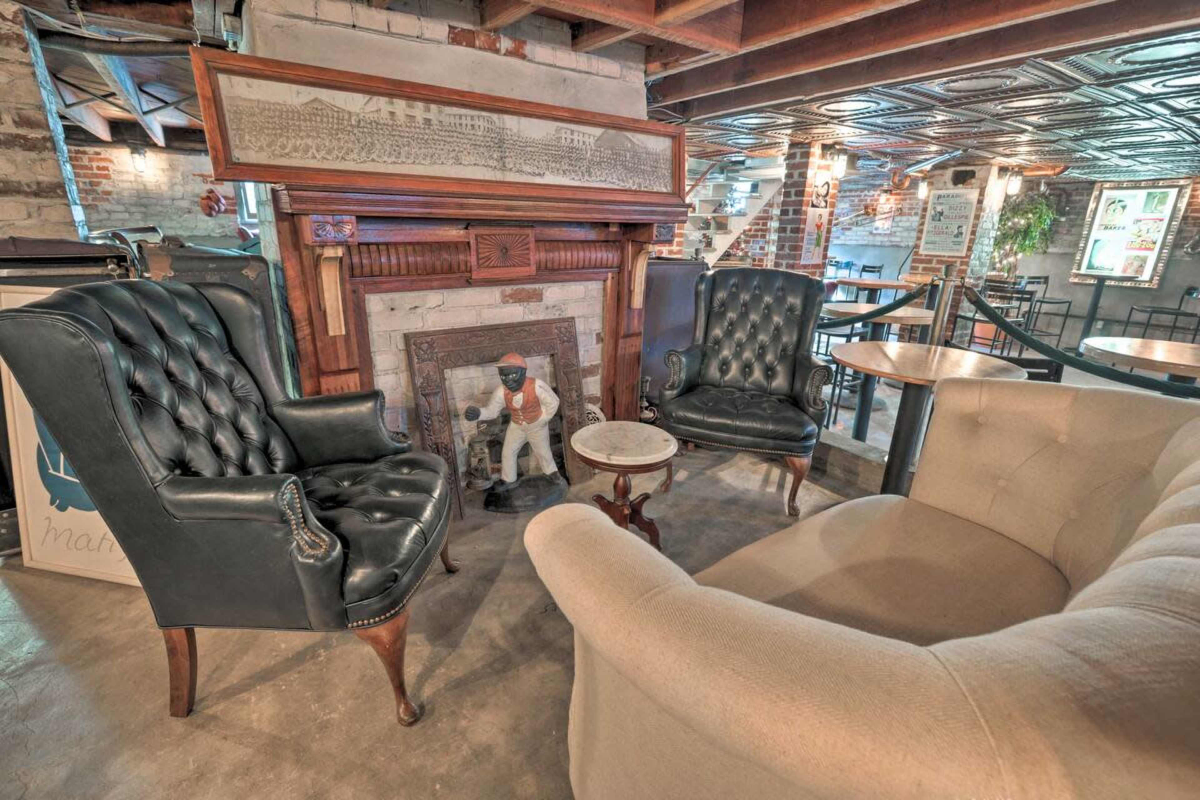A cozy seating area with two leather armchairs and a light-colored sofa arranged around a small table in front of a decorative fireplace featuring an ornate mantel and a statue.