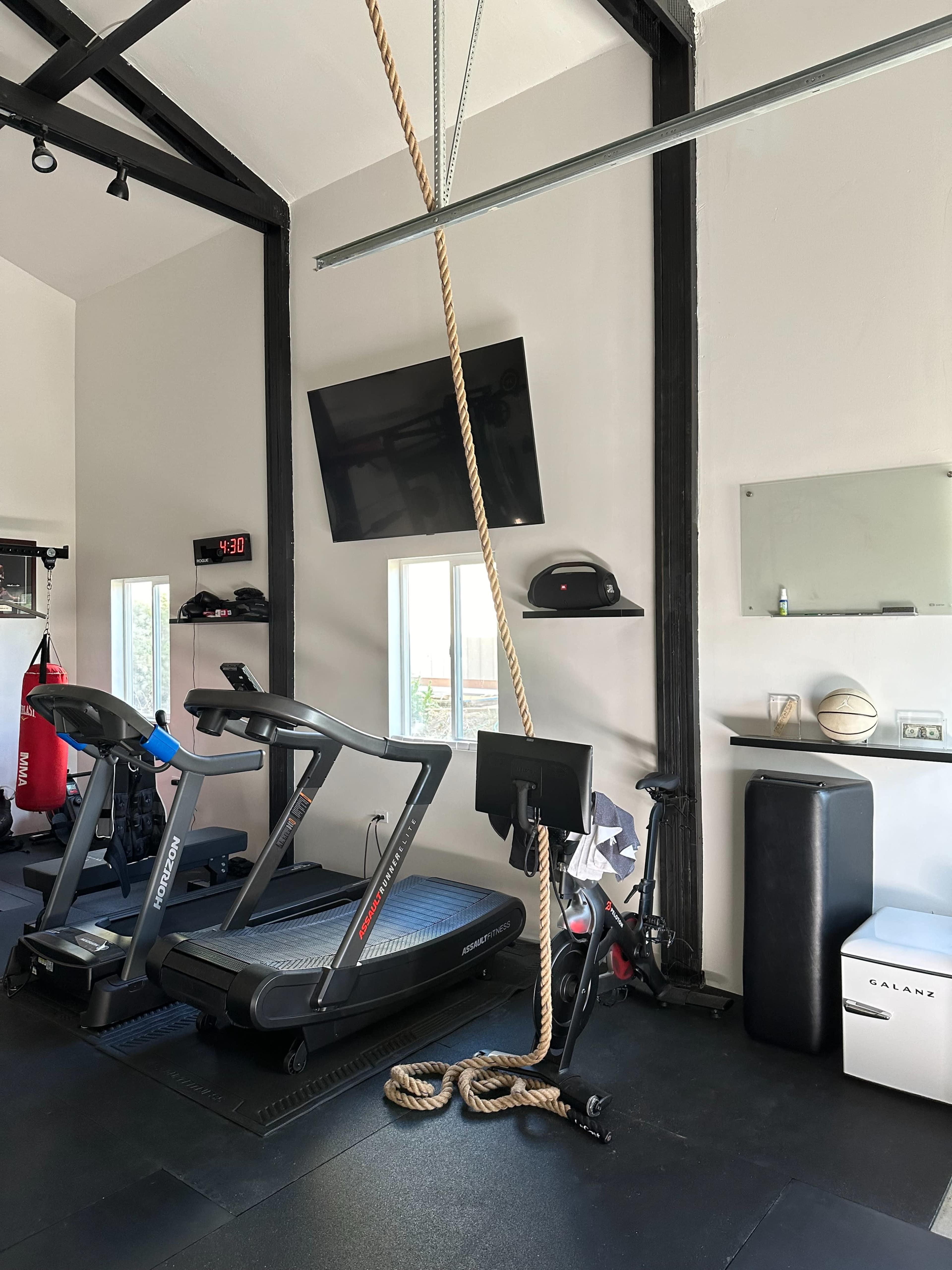 The image shows a home gym featuring a treadmill, an exercise bike, a punching bag, and a hanging rope.