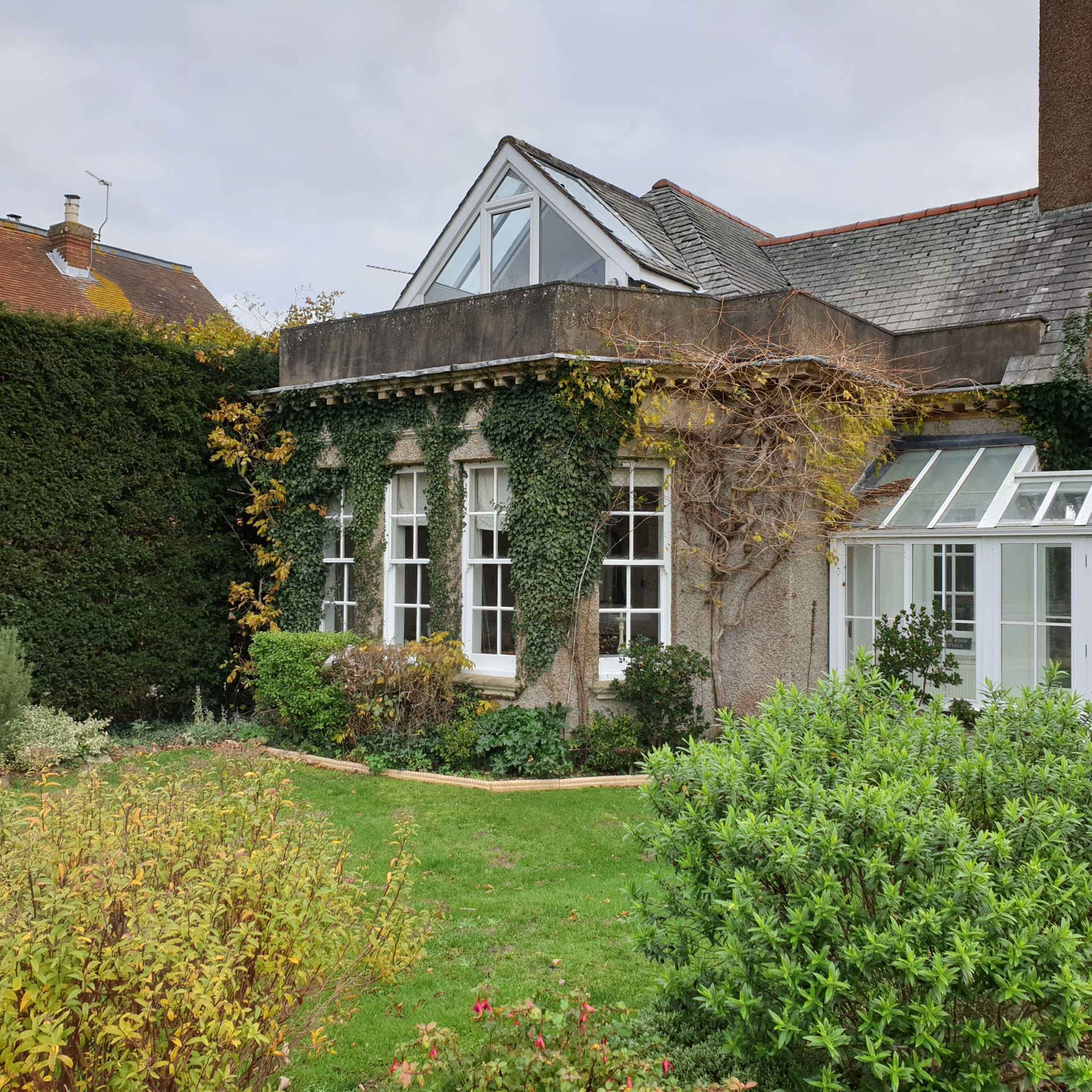 A house with a garden features a vine-covered exterior and a glass conservatory.