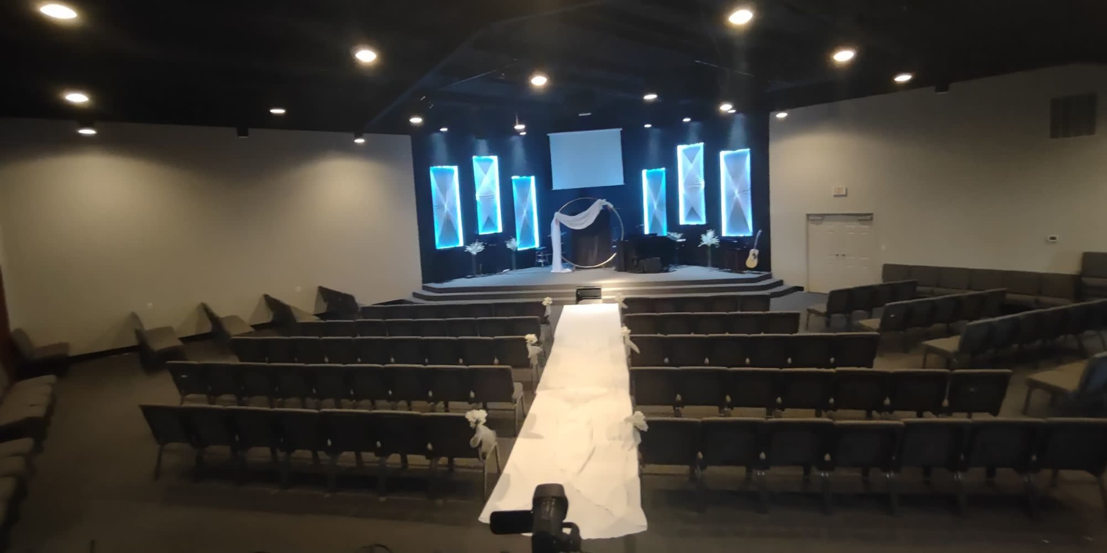 A spacious auditorium set up for an event, featuring rows of chairs facing a stage adorned with blue lighting and decorative elements.