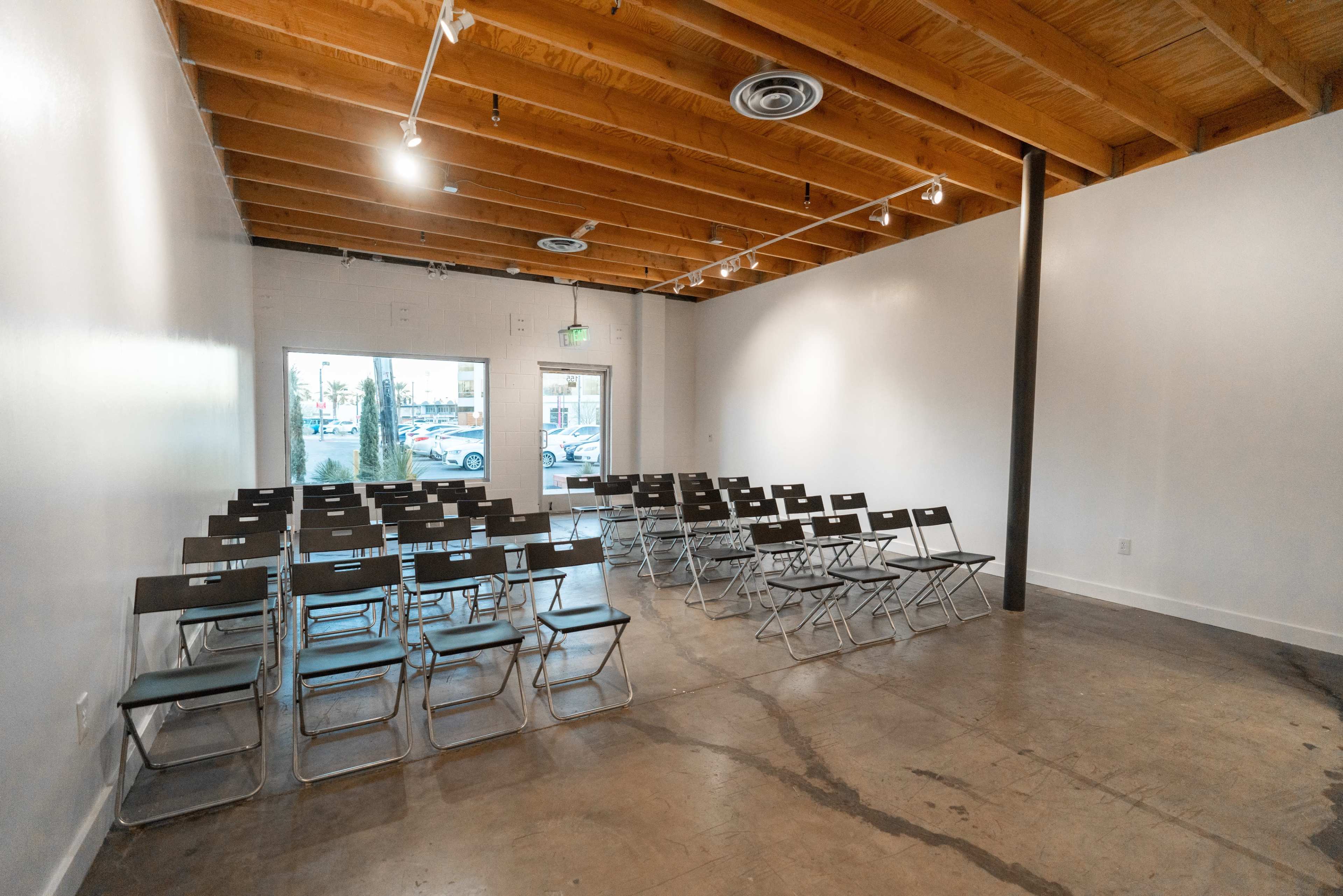 A minimalist room with rows of black folding chairs arranged facing a large window.