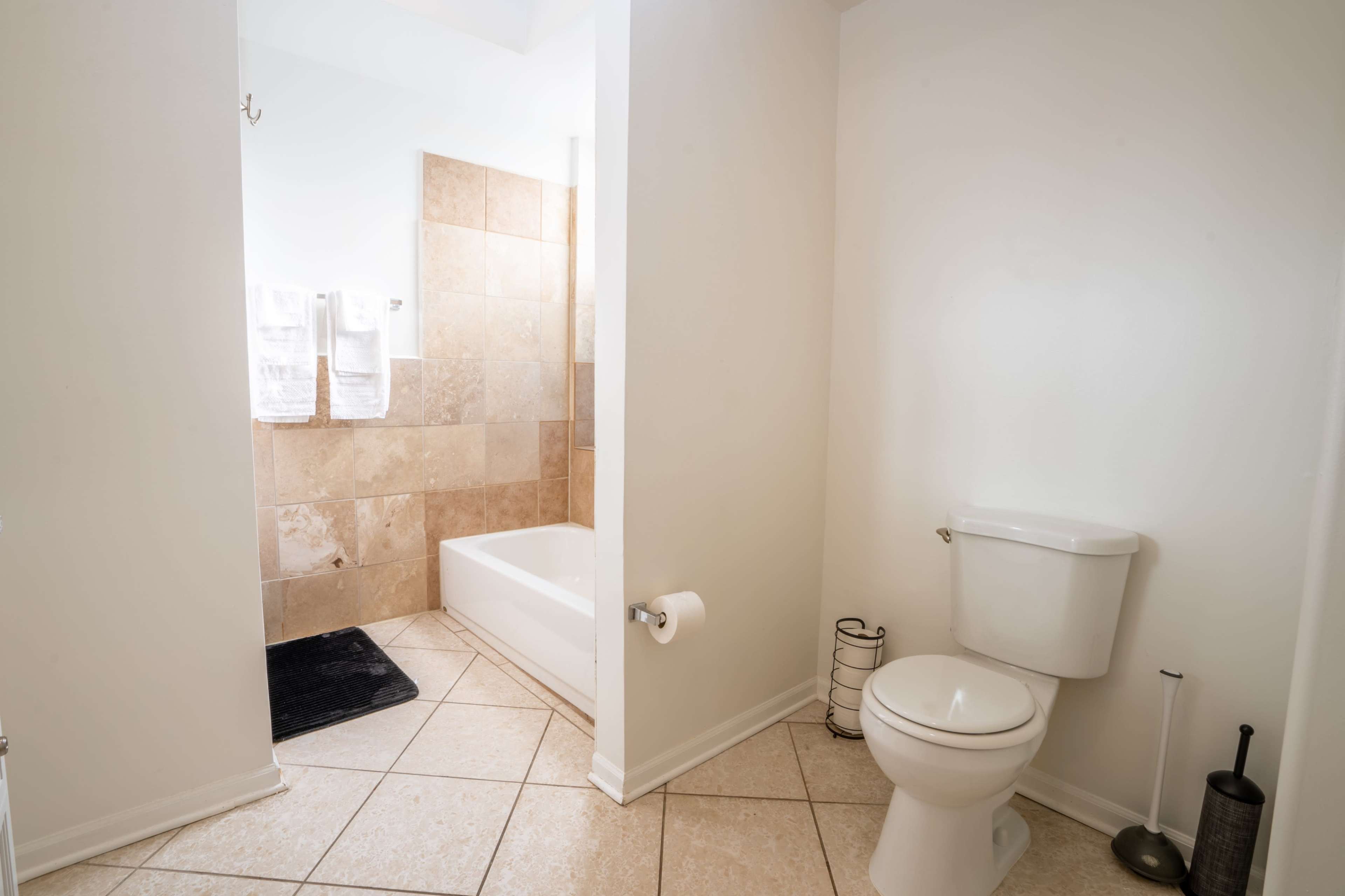 A simple bathroom featuring a toilet, a bathtub with a shower, and beige tiled walls.