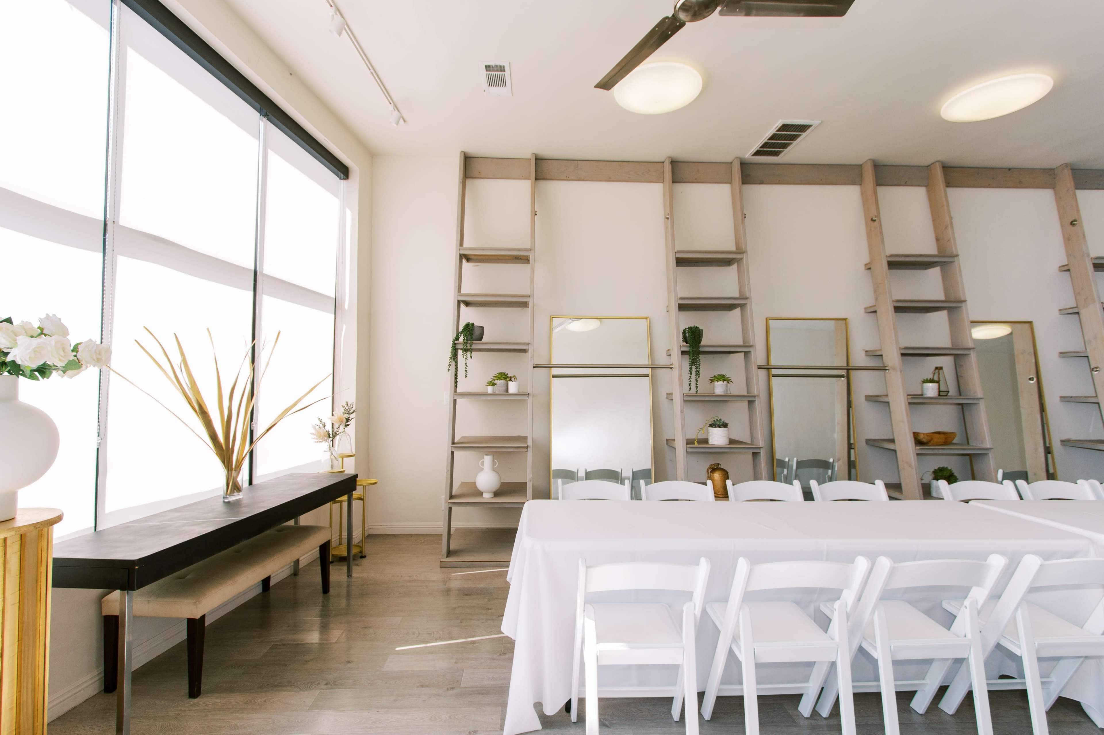 A bright meeting room with a long table set for a gathering, complemented by modern shelving and plants along the walls.