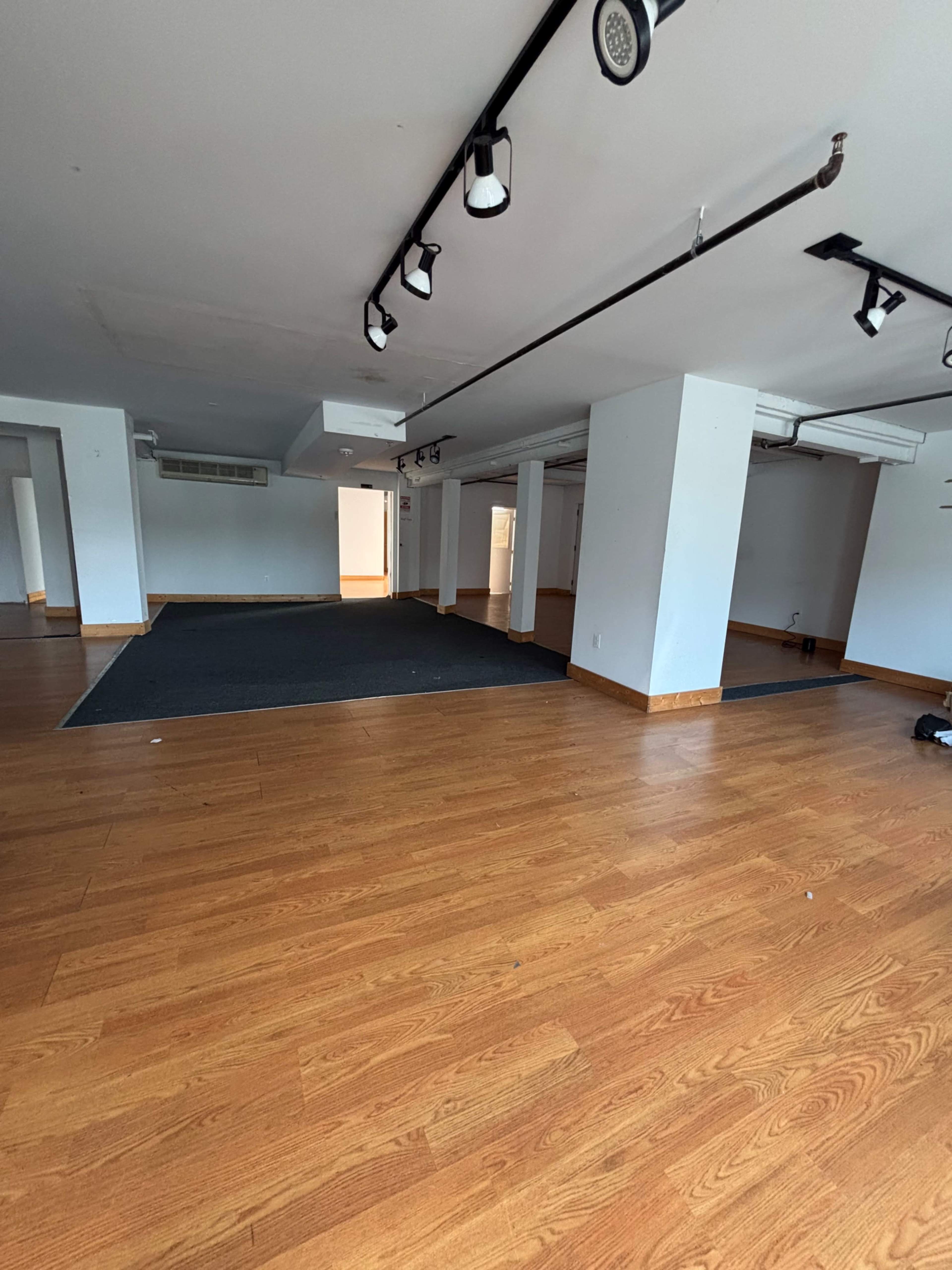 The image shows an empty interior space with wood flooring, bright overhead lights, and several partitions.