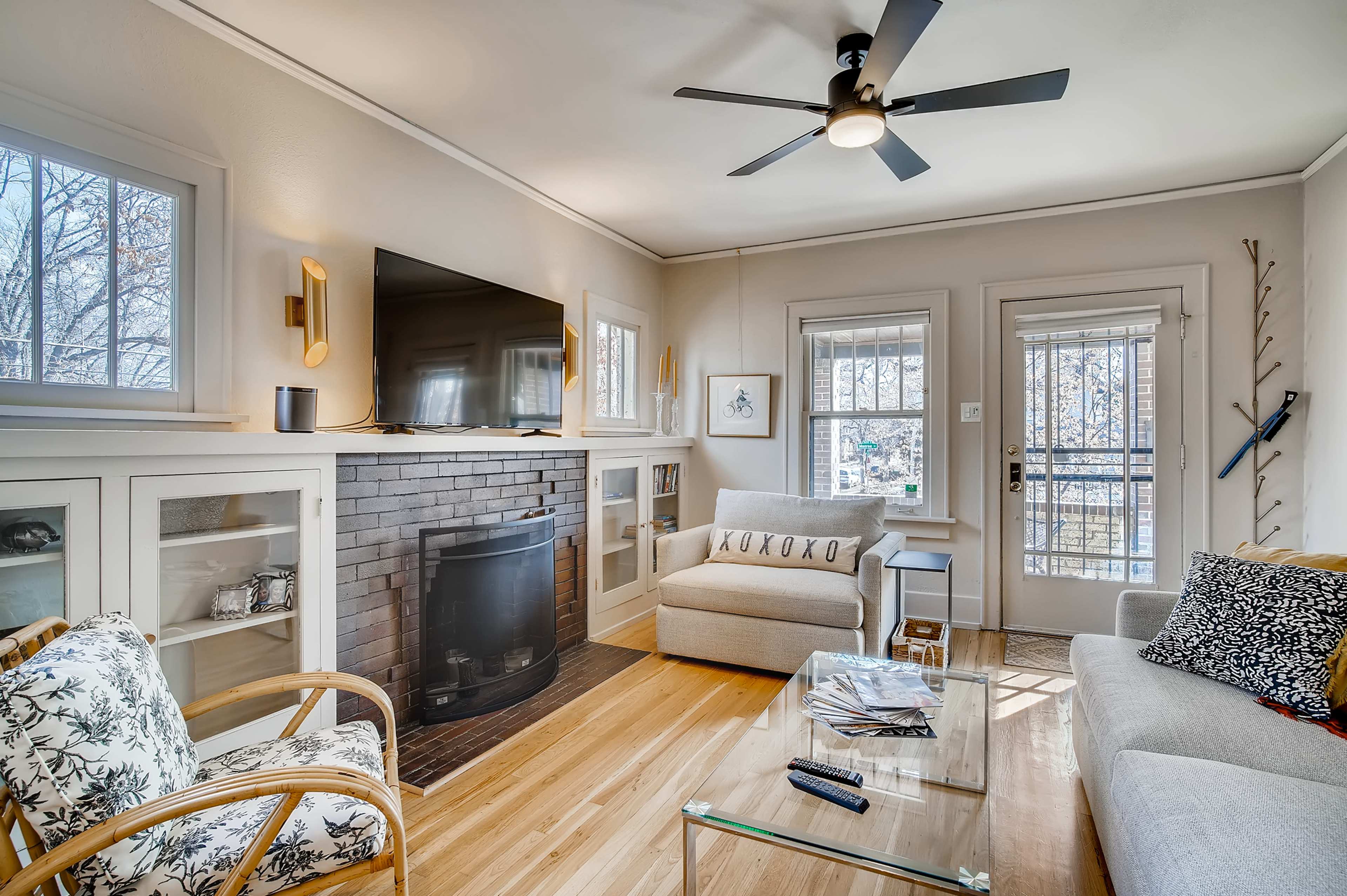 The living room features a fireplace, a television mounted on the wall, and a mix of seating options with large windows allowing natural light.