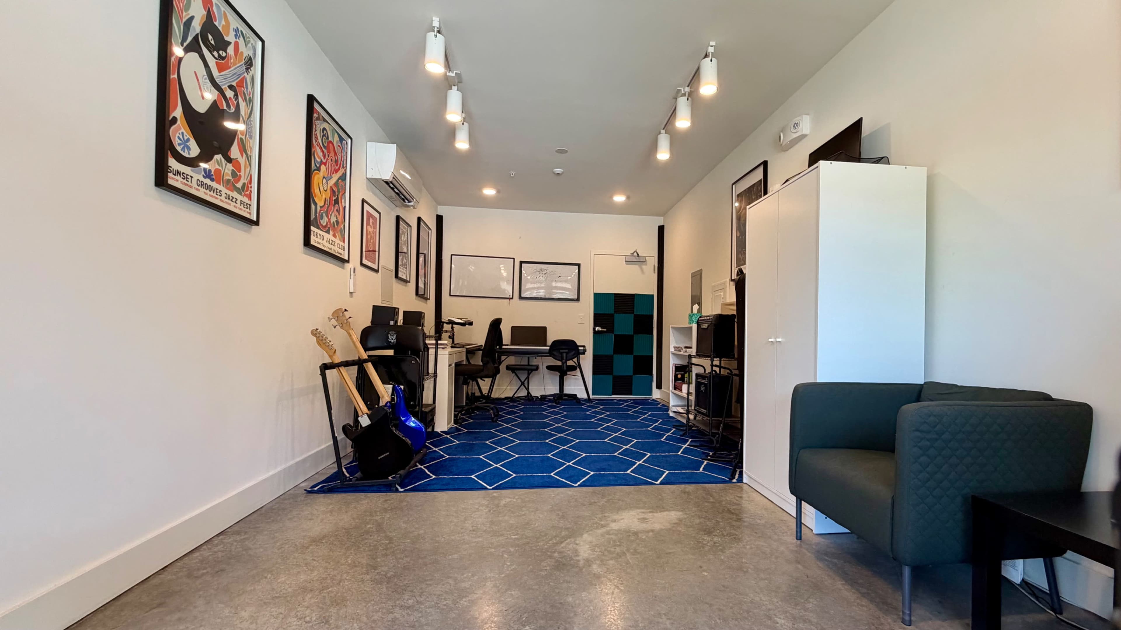 The image shows a modern music practice room featuring guitars, office chairs, a desk, and colorful wall art.