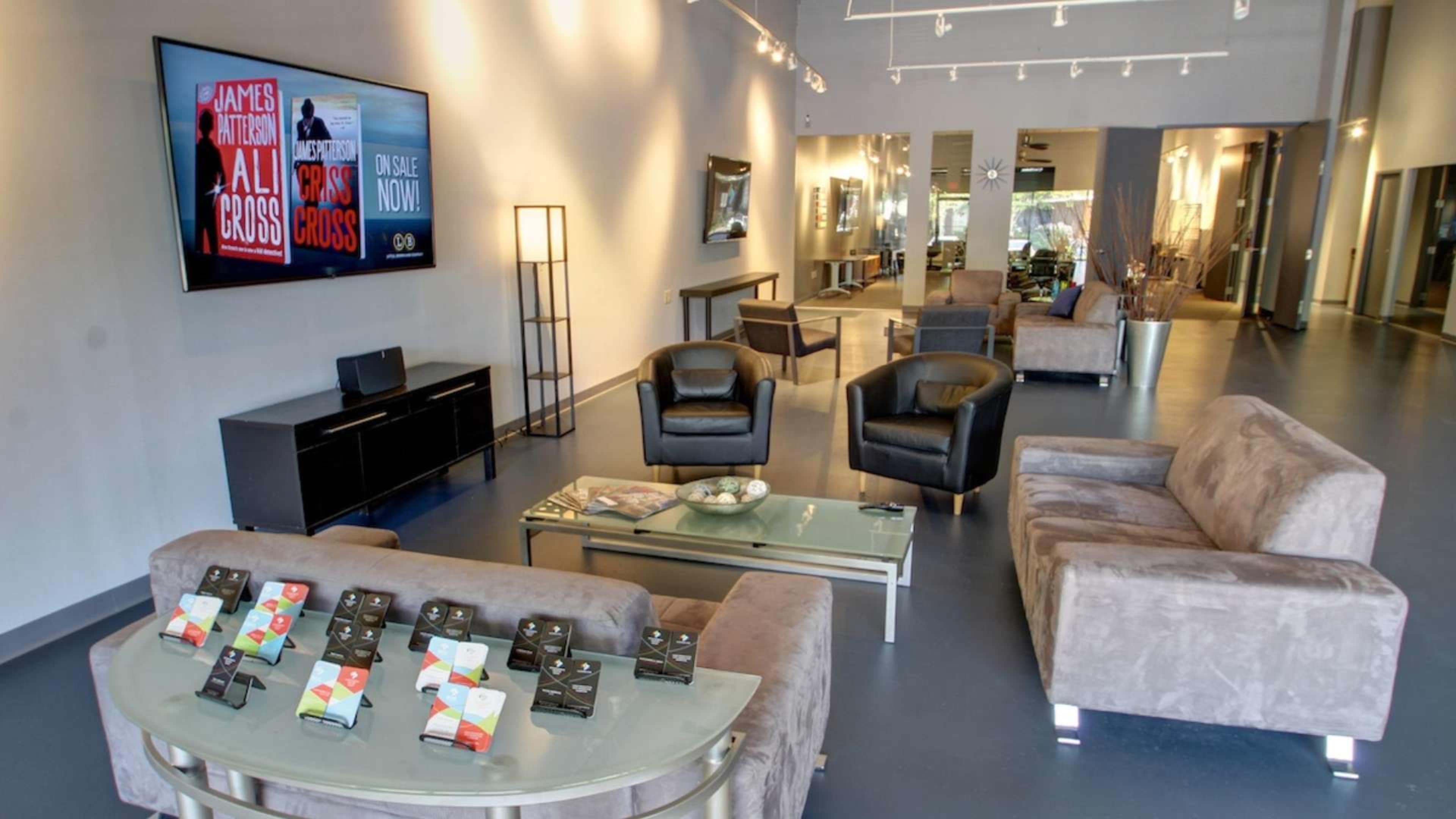 A modern waiting area with leather chairs, a glass table displaying items, and a large screen on the wall.