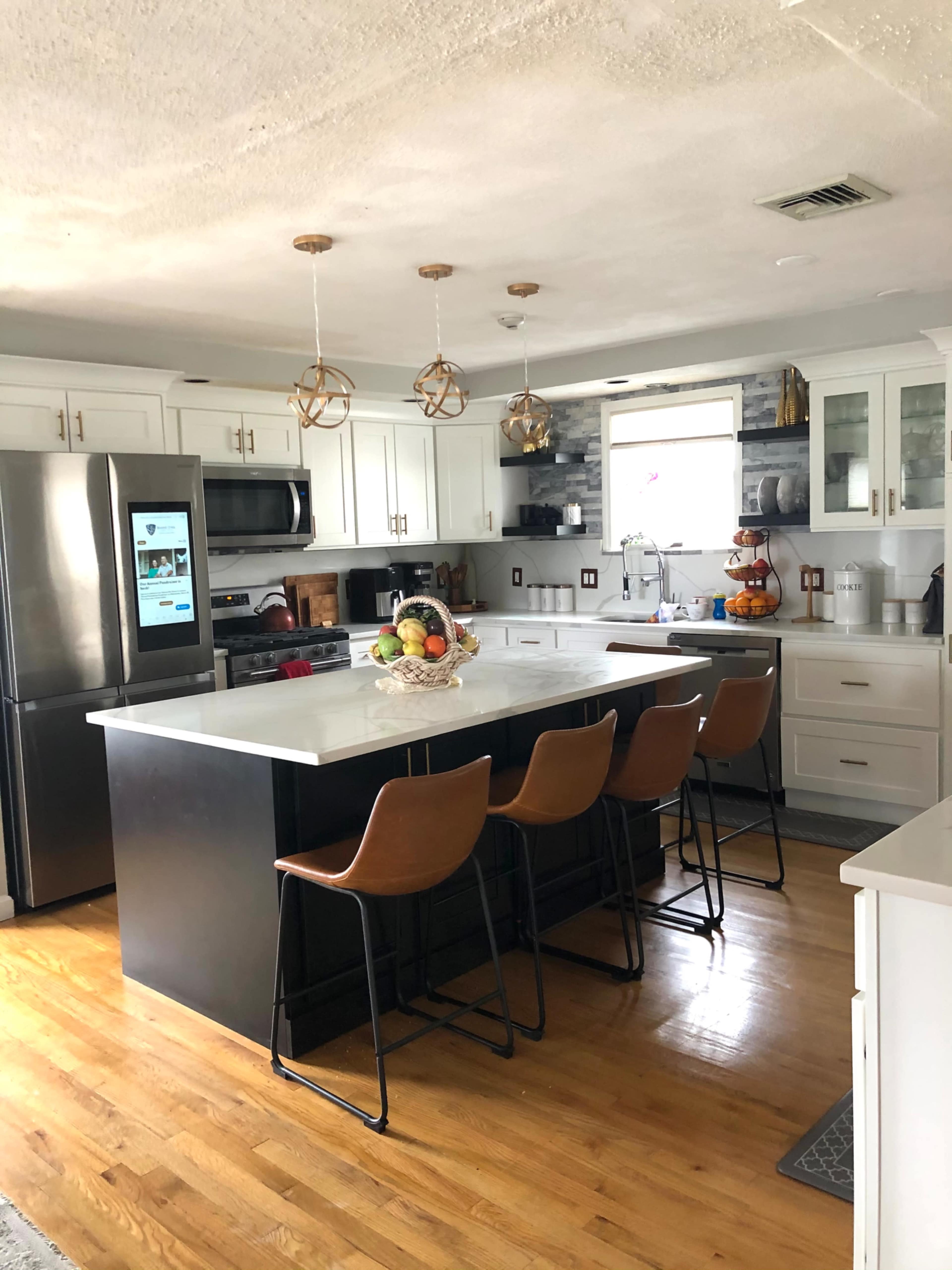 A modern kitchen features white cabinets, a large island with bar stools, and stainless steel appliances.