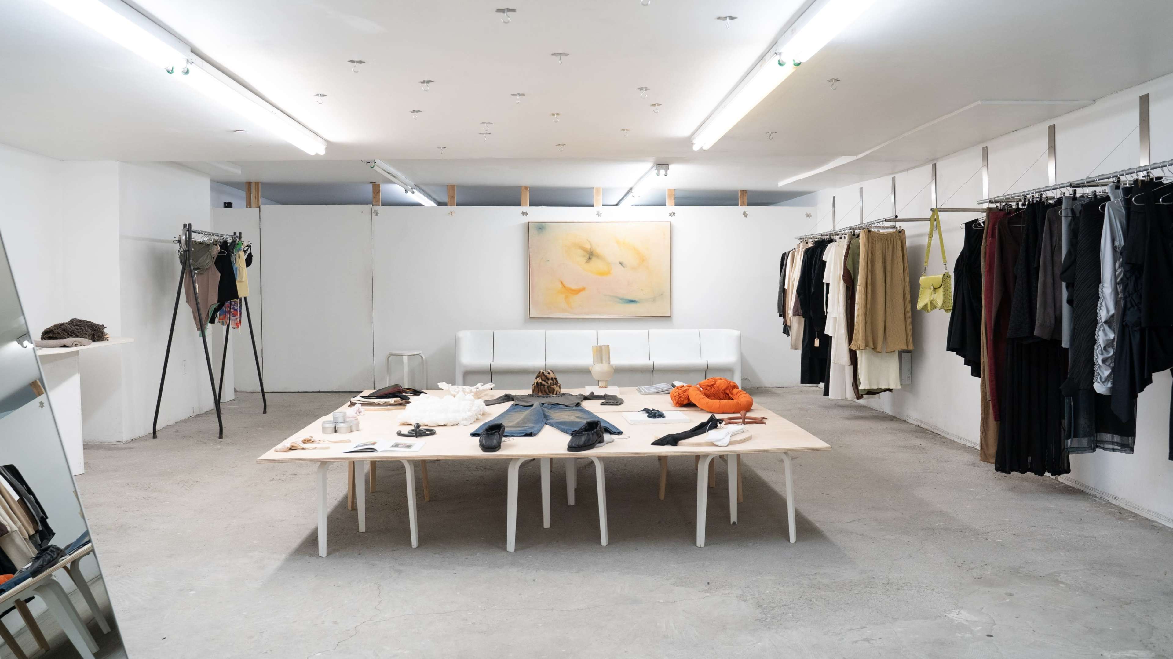 A minimalist clothing boutique with a central table displaying various fashion items and adjacent racks holding garments.
