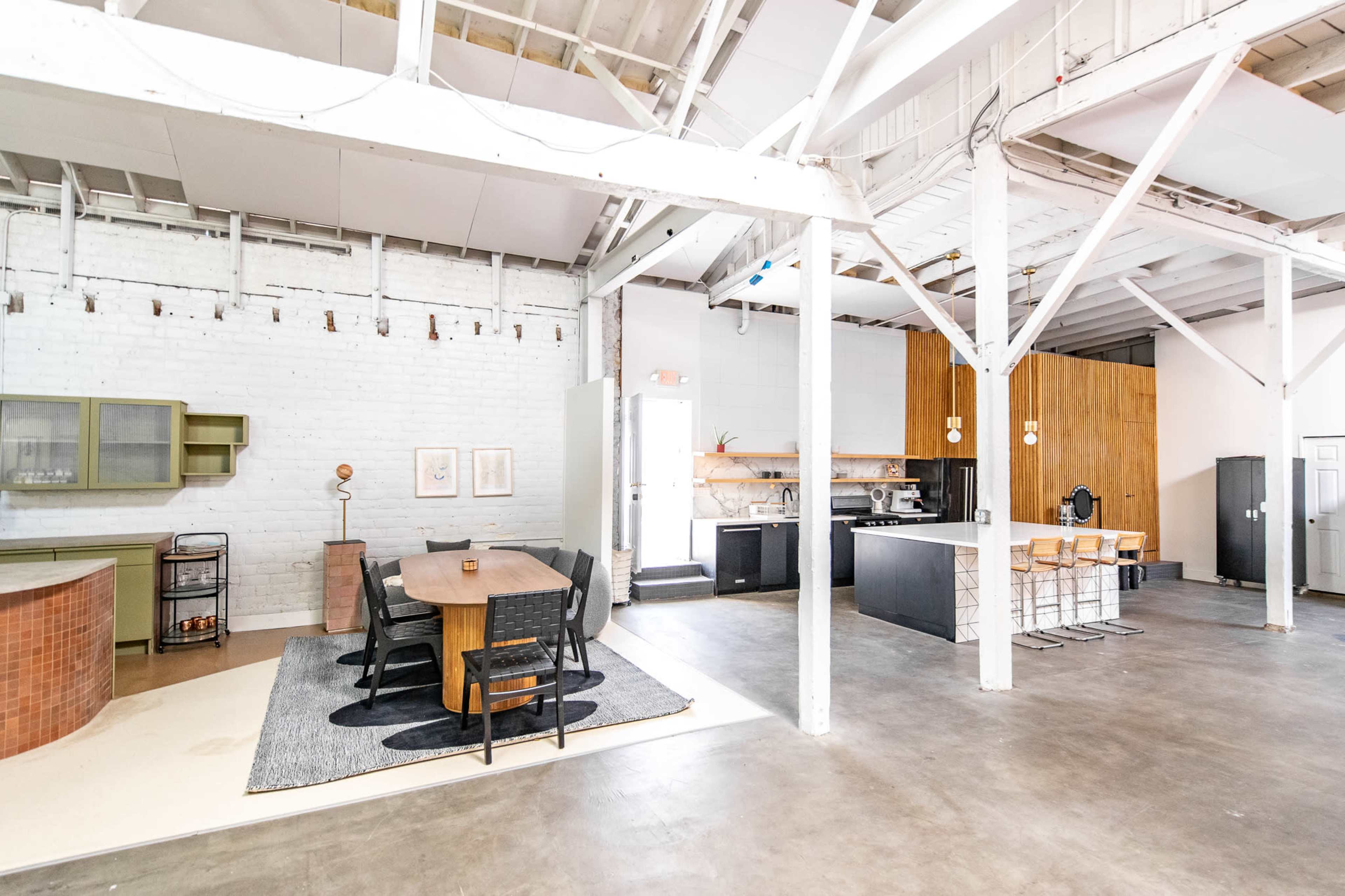 A spacious, open-plan area with a dining table, kitchen, and seating, featuring high ceilings and industrial-style decor.