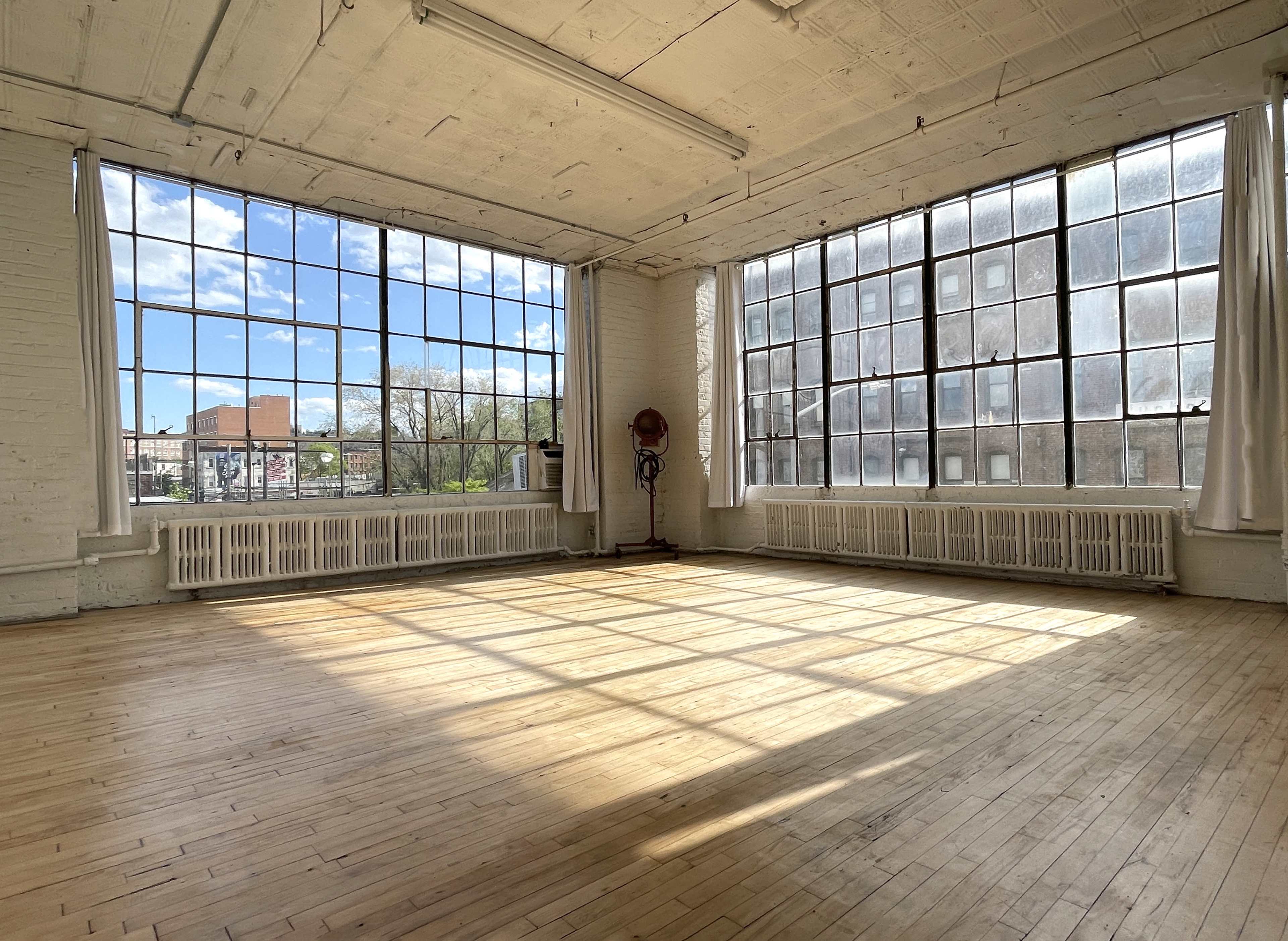 A spacious, empty room with large windows allowing natural light to fill the wooden floor.