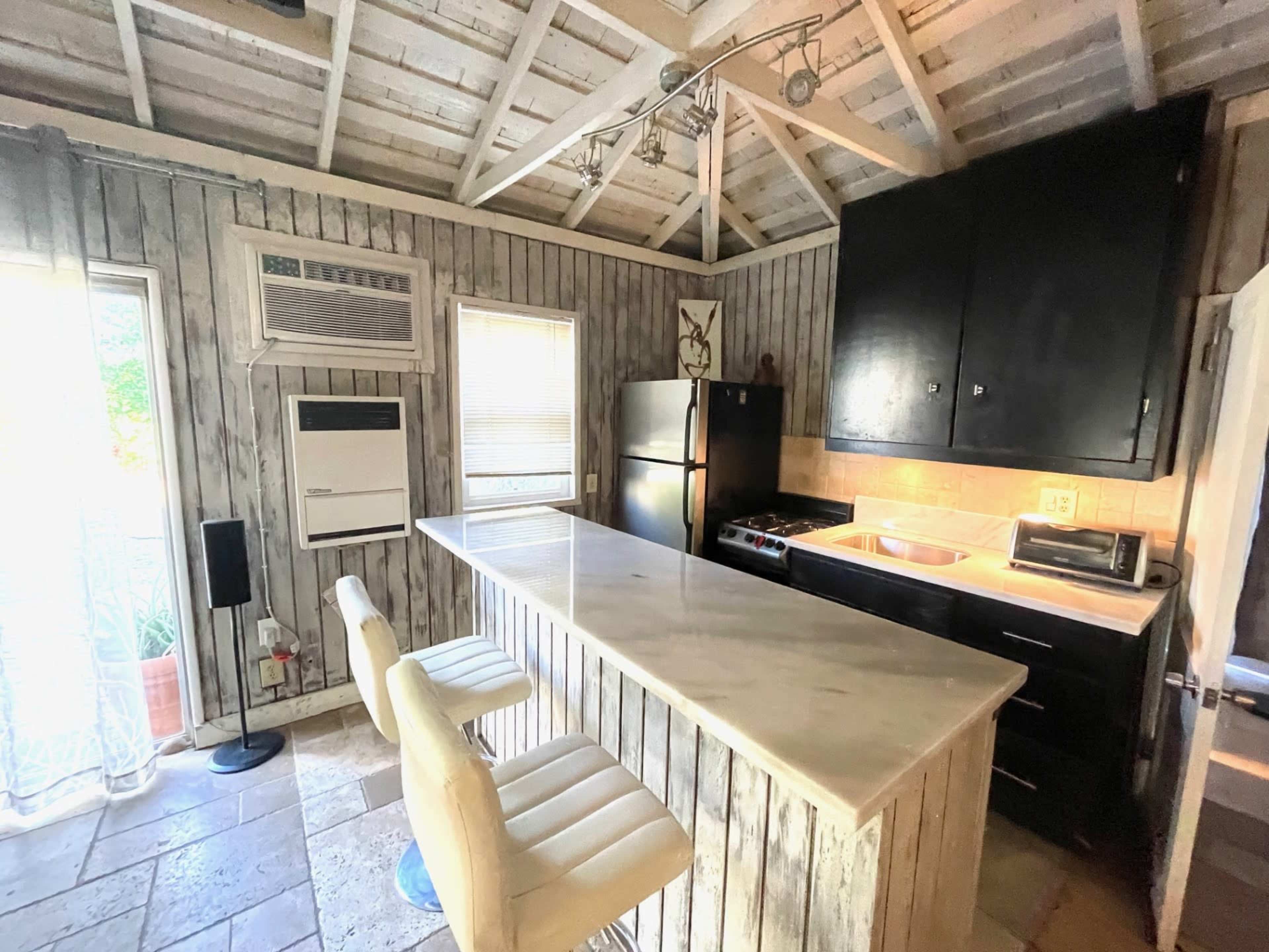 A rustic kitchen with wooden walls, a marble-topped island with two white bar stools, and modern appliances including a refrigerator and a stove.