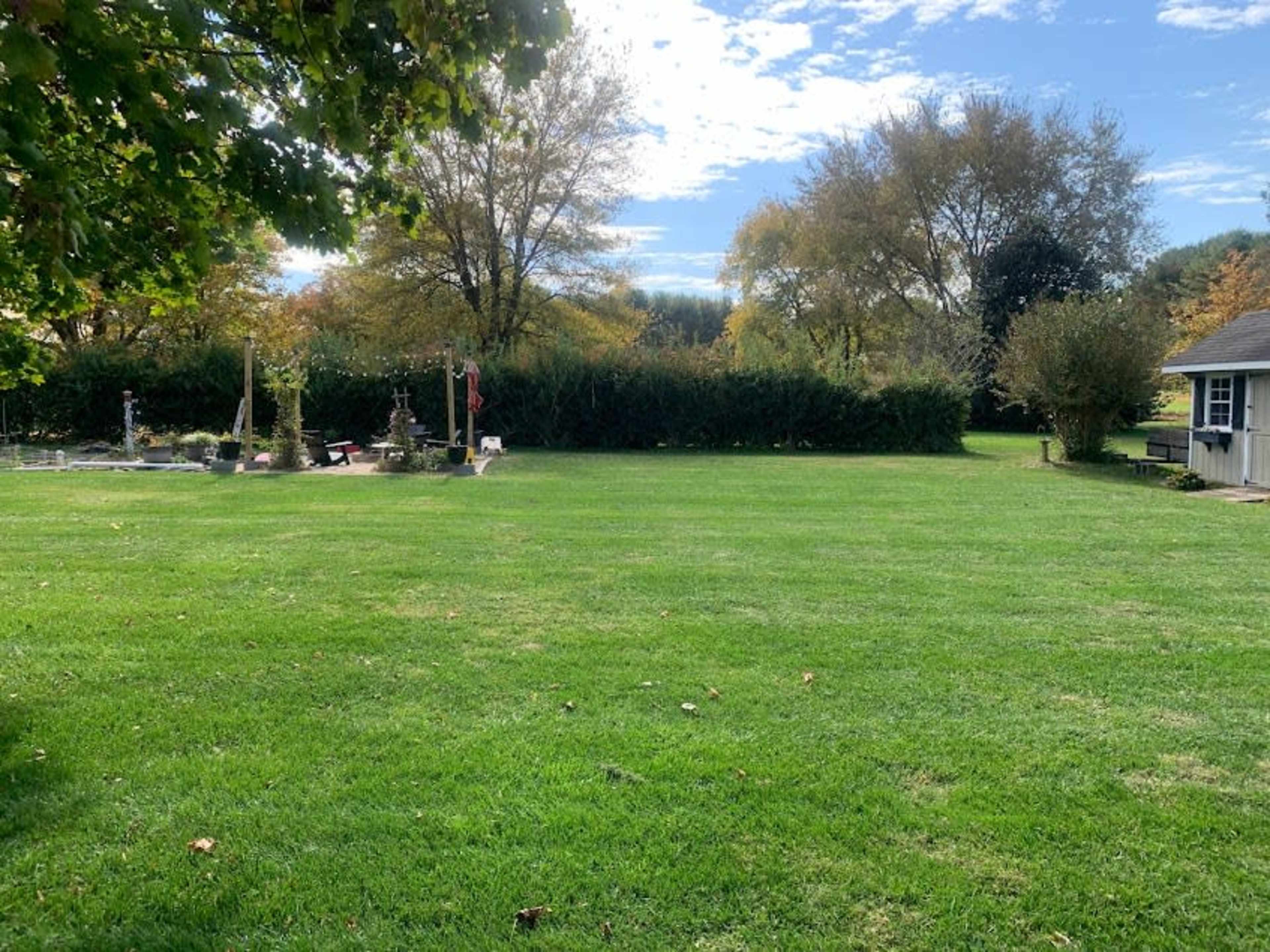 A large, well-maintained grassy area surrounded by trees and shrubs, with a few garden features visible in the background.