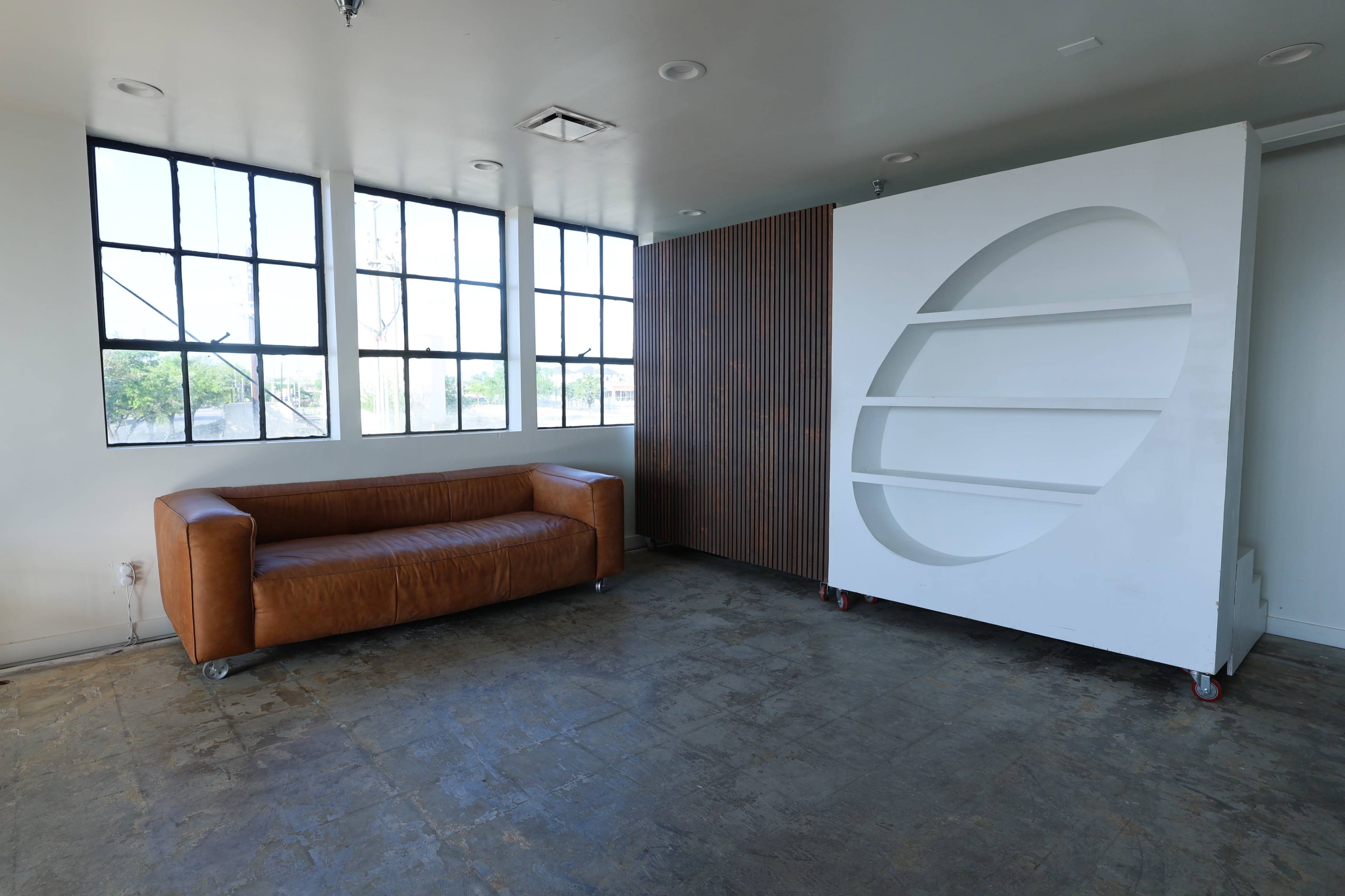 The image shows a minimalist room with a brown leather couch on one side and a large white shelving unit on wheels against the wall.