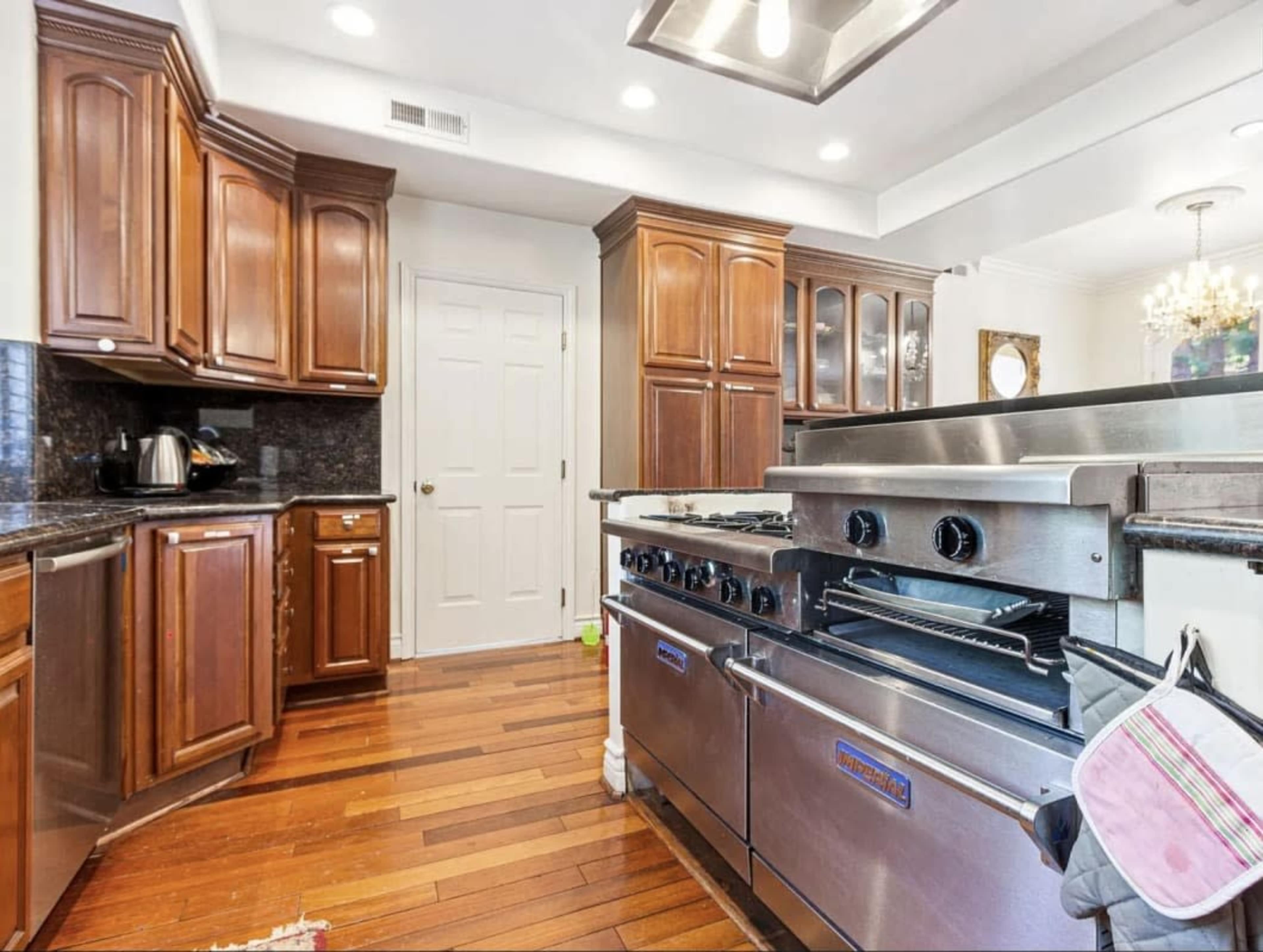 The image shows a kitchen with dark wooden cabinets, a stainless steel range, and hardwood flooring.