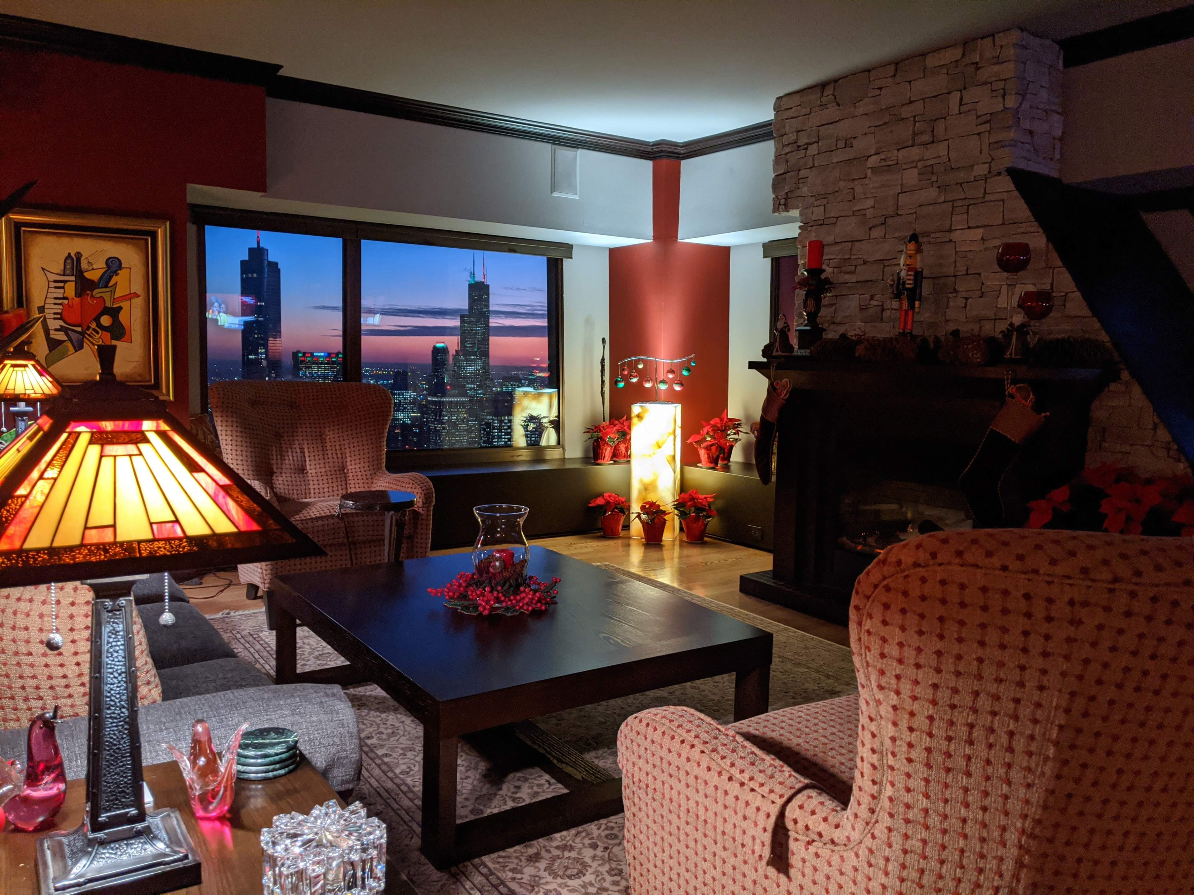 A cozy living room with a fireplace and a view of the Chicago skyline at sunset, decorated with holiday accents.