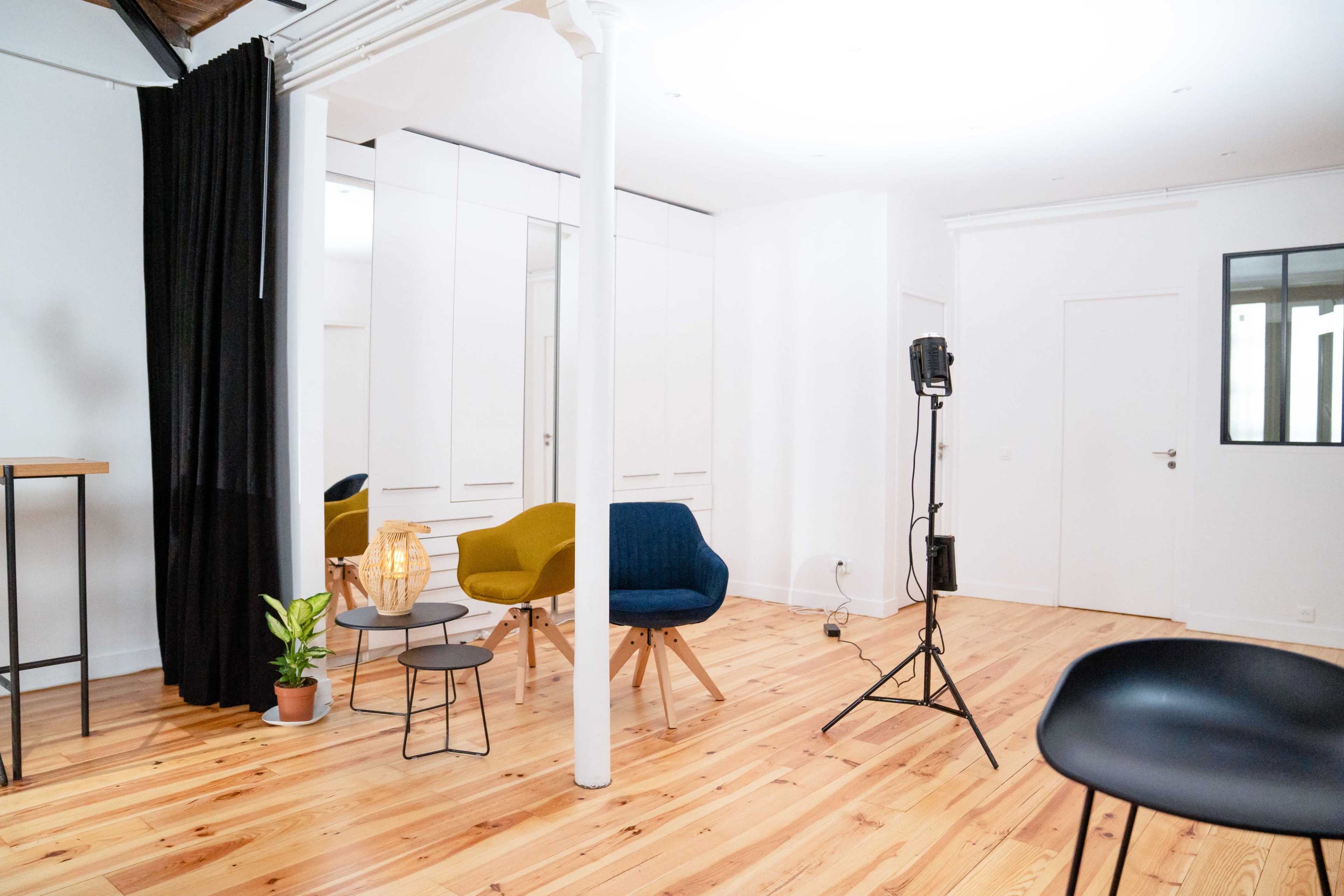 A modern, minimalistic interior space featuring a combination of chairs, a small table, a plant, and a lighting setup.