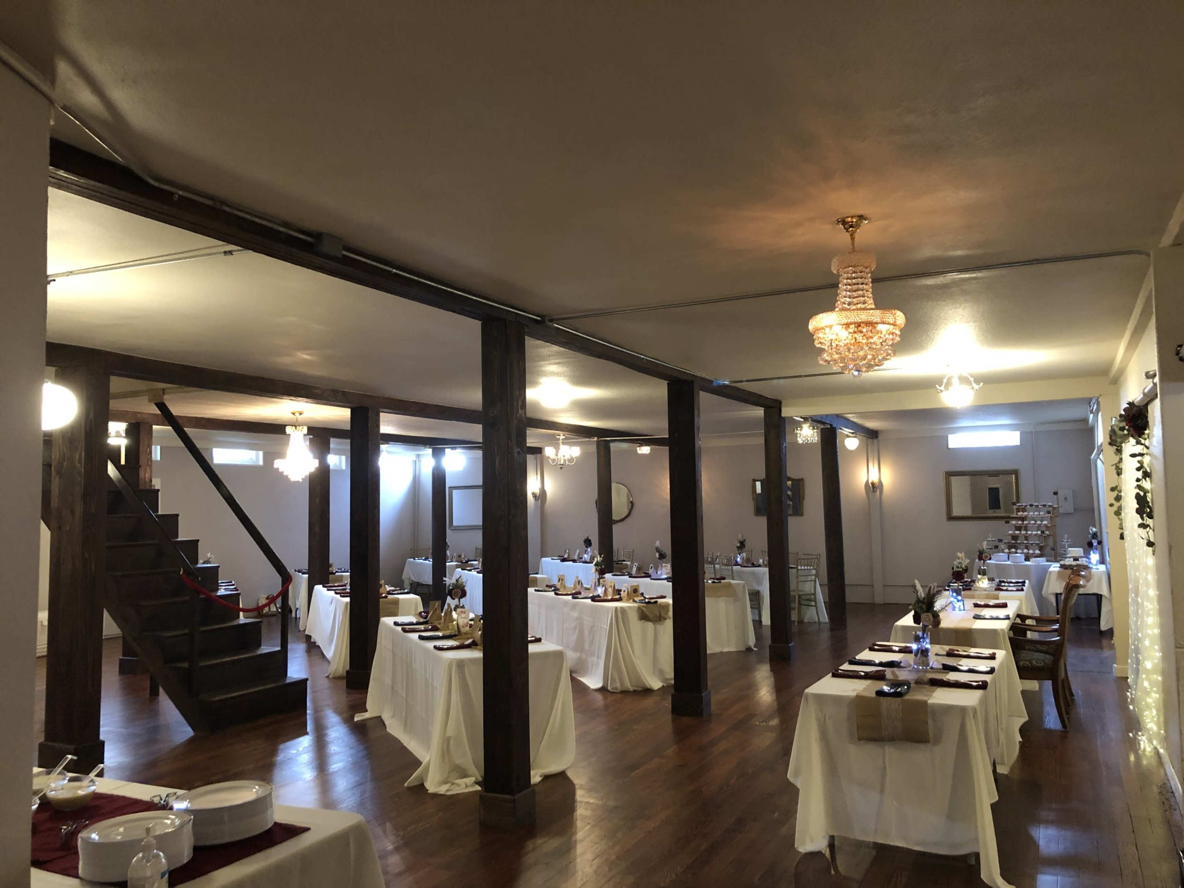 A spacious banquet hall with neatly arranged tables covered in white tablecloths and a staircase in the background.