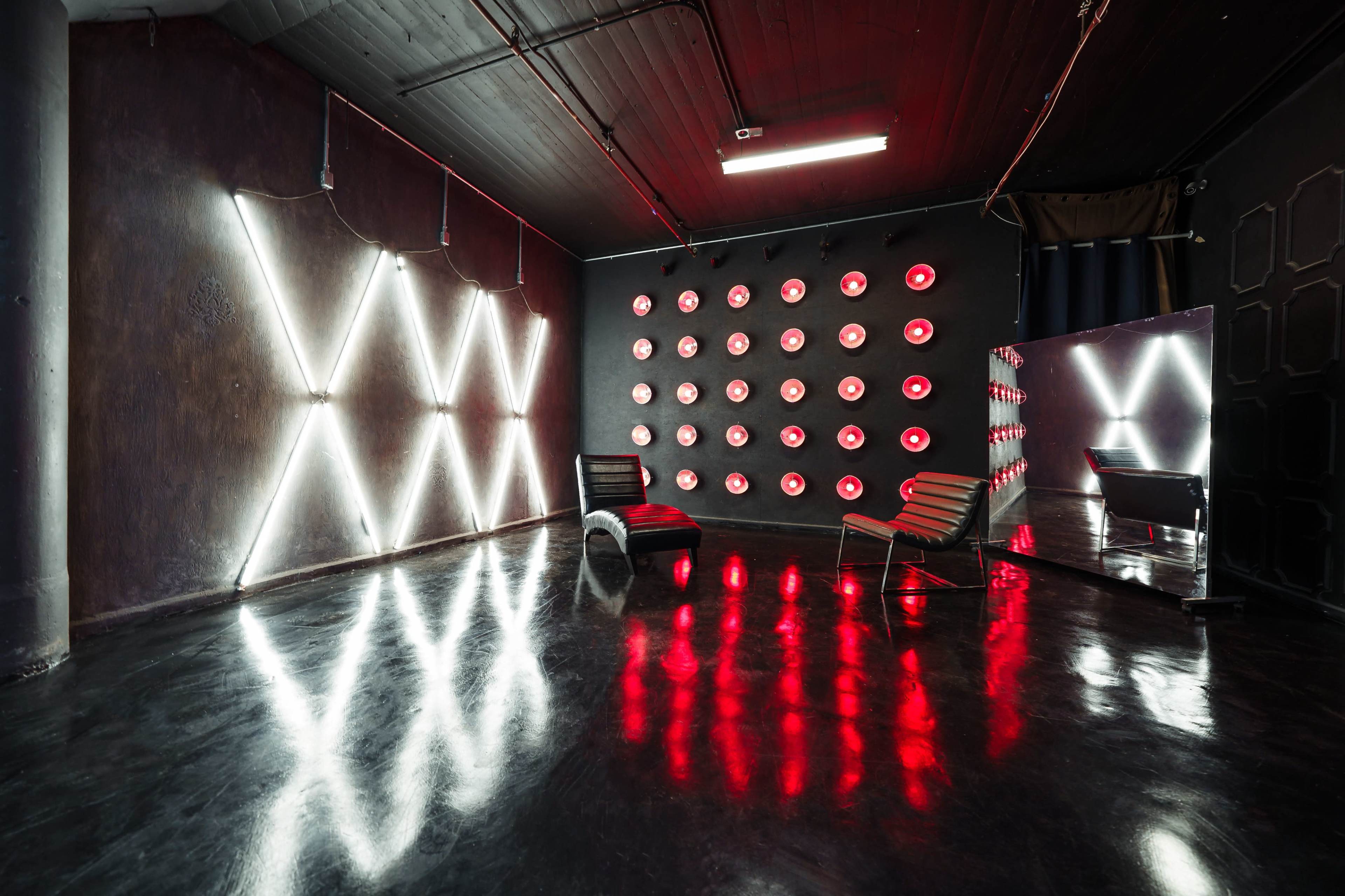The room features a dark floor with geometric light installations and a modern chair against the walls adorned with circular red lights.