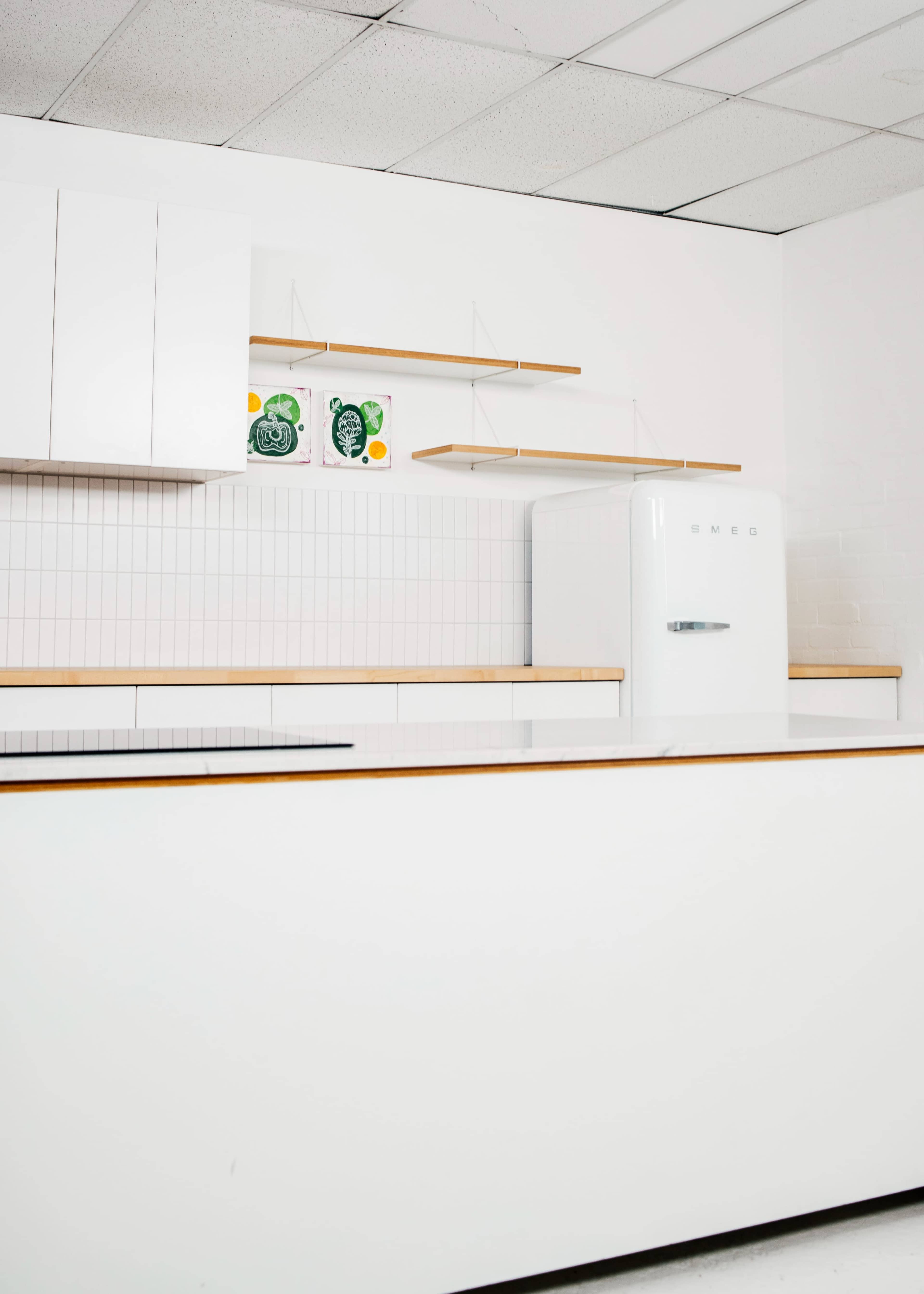 A bright kitchen features a white refrigerator, white cabinetry, and open shelving with two decorated plates on display.