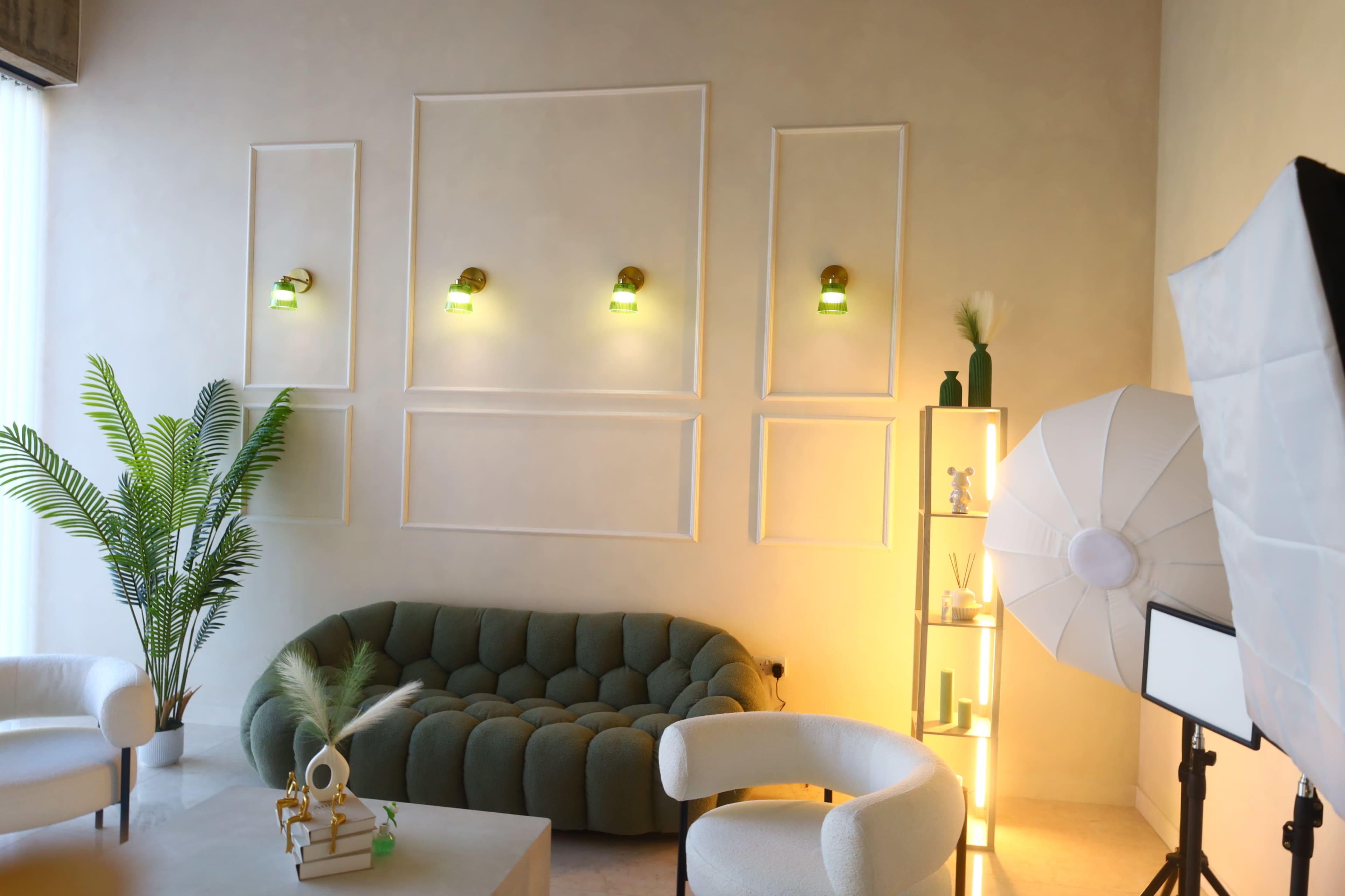 The scene features a modern living area with a green sofa, two white chairs, four wall sconces, and a floor plant, illuminated by soft lighting.