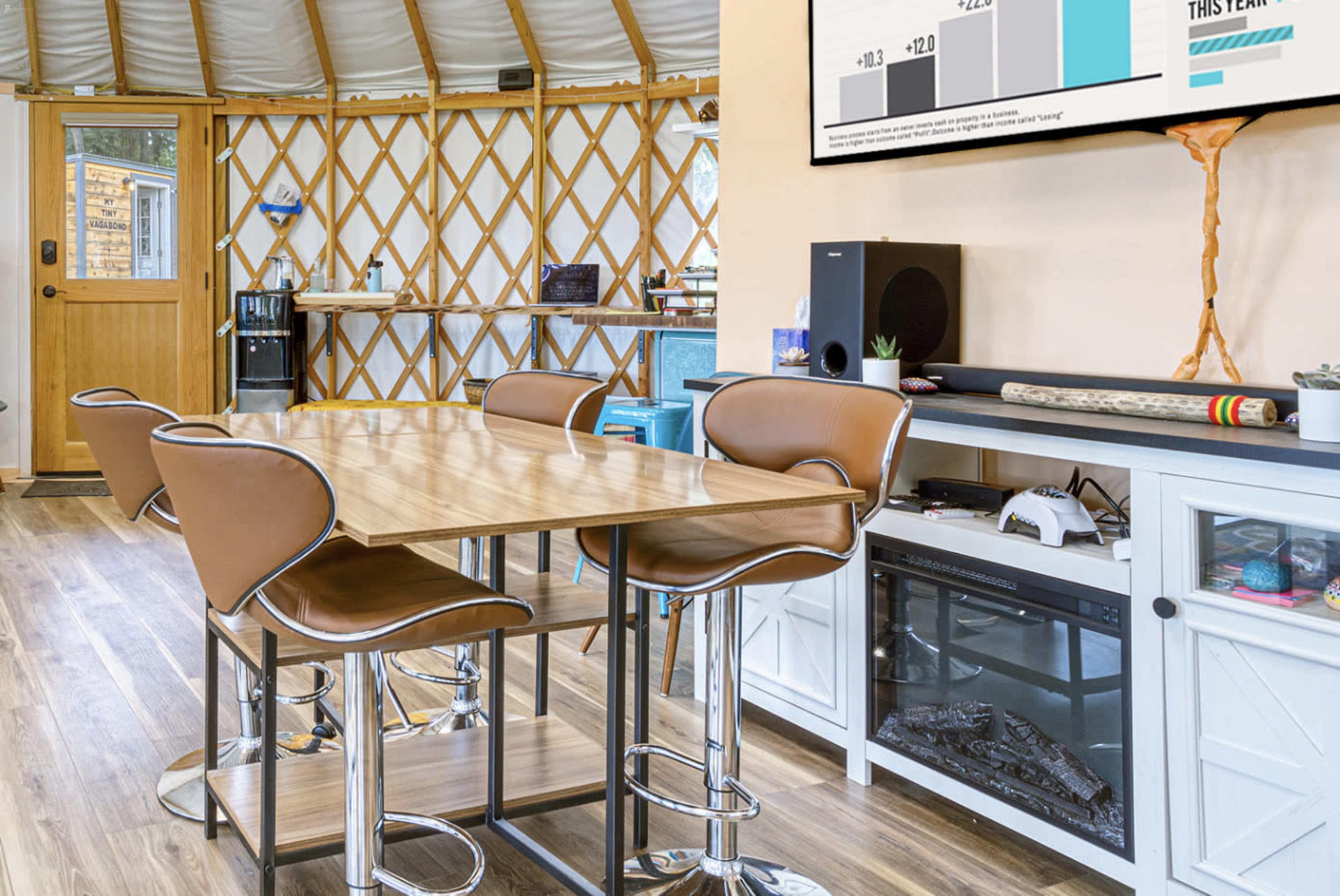 A modern interior space with a wooden table and brown chairs, featuring a wall-mounted screen, a sound system, and a door leading outside.