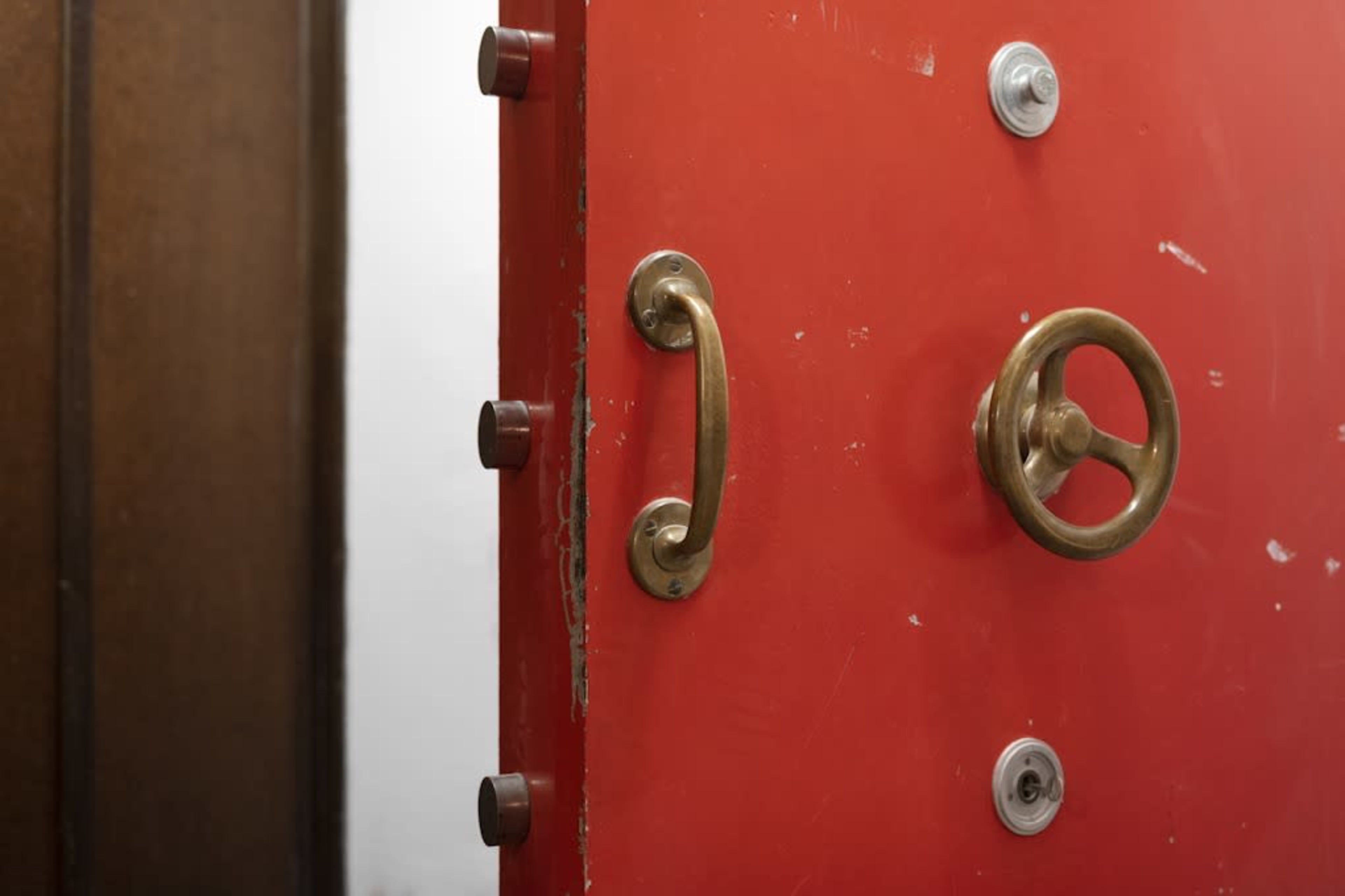 A red door with a brass handle and a circular lock is partially open, revealing a wooden door beside it.