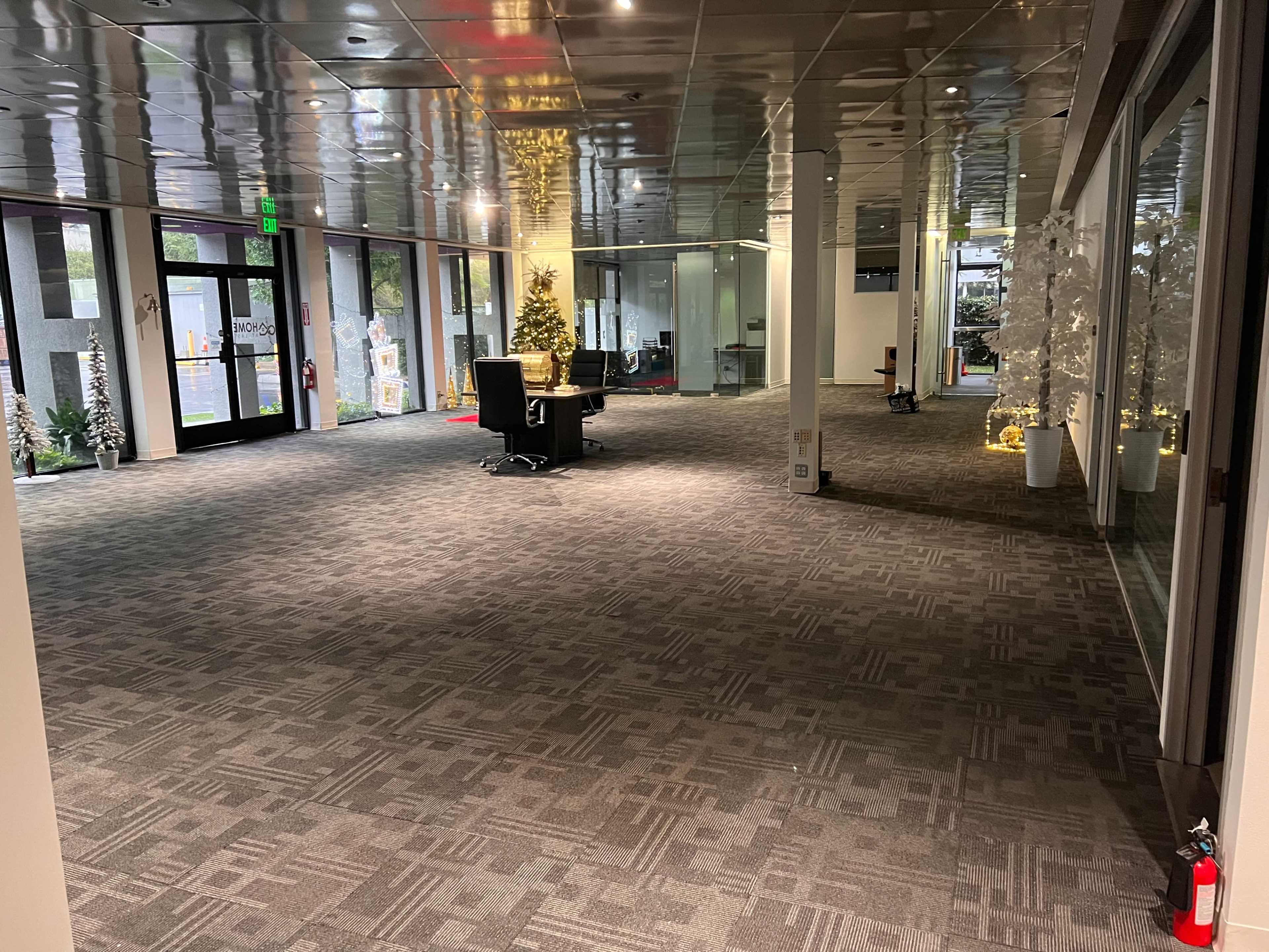 A spacious, empty office lobby decorated with Christmas trees and white decorations, featuring a reception area with a chair and a fire extinguisher on the wall.