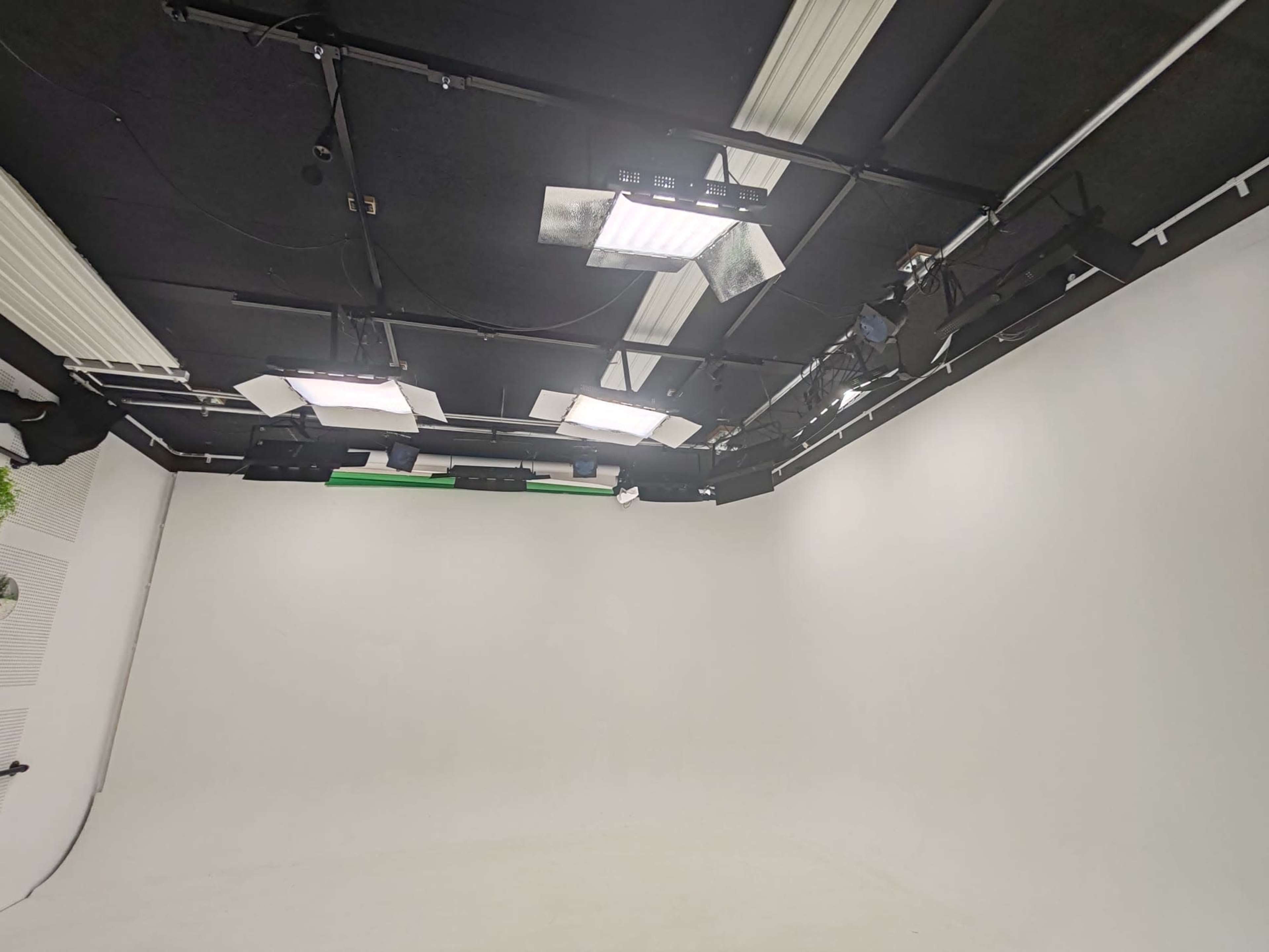The image shows a professional photography studio with a large, white backdrop and various lighting equipment mounted on the ceiling.