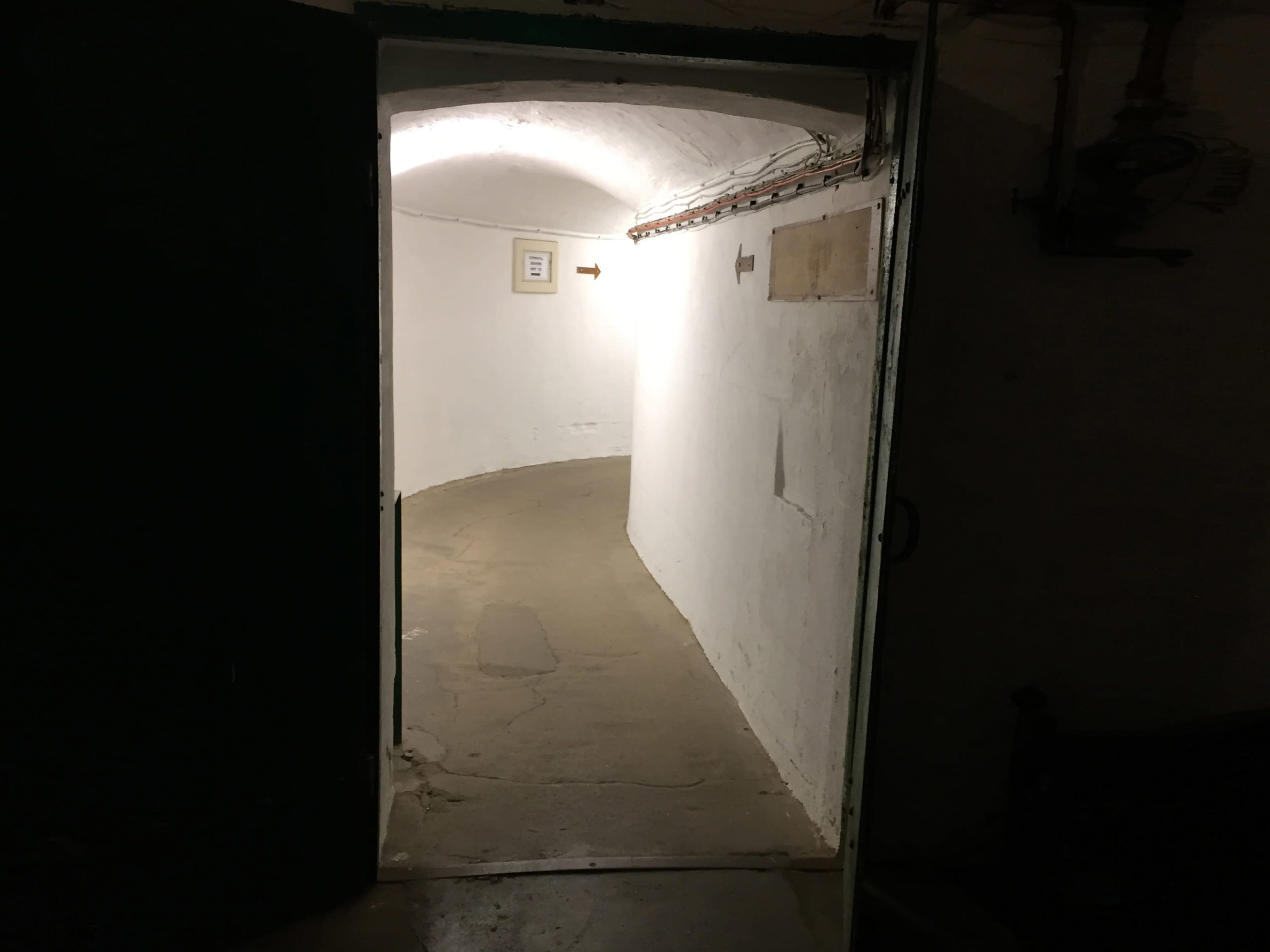 A dimly lit arched corridor leads from an open door into a white-walled, curved passageway.